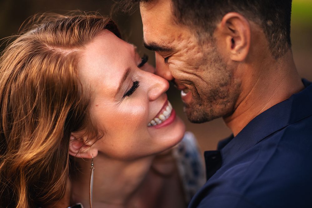 Close-up of smiling redhead woman and dark-haired man nearly touching foreheads outdoors.