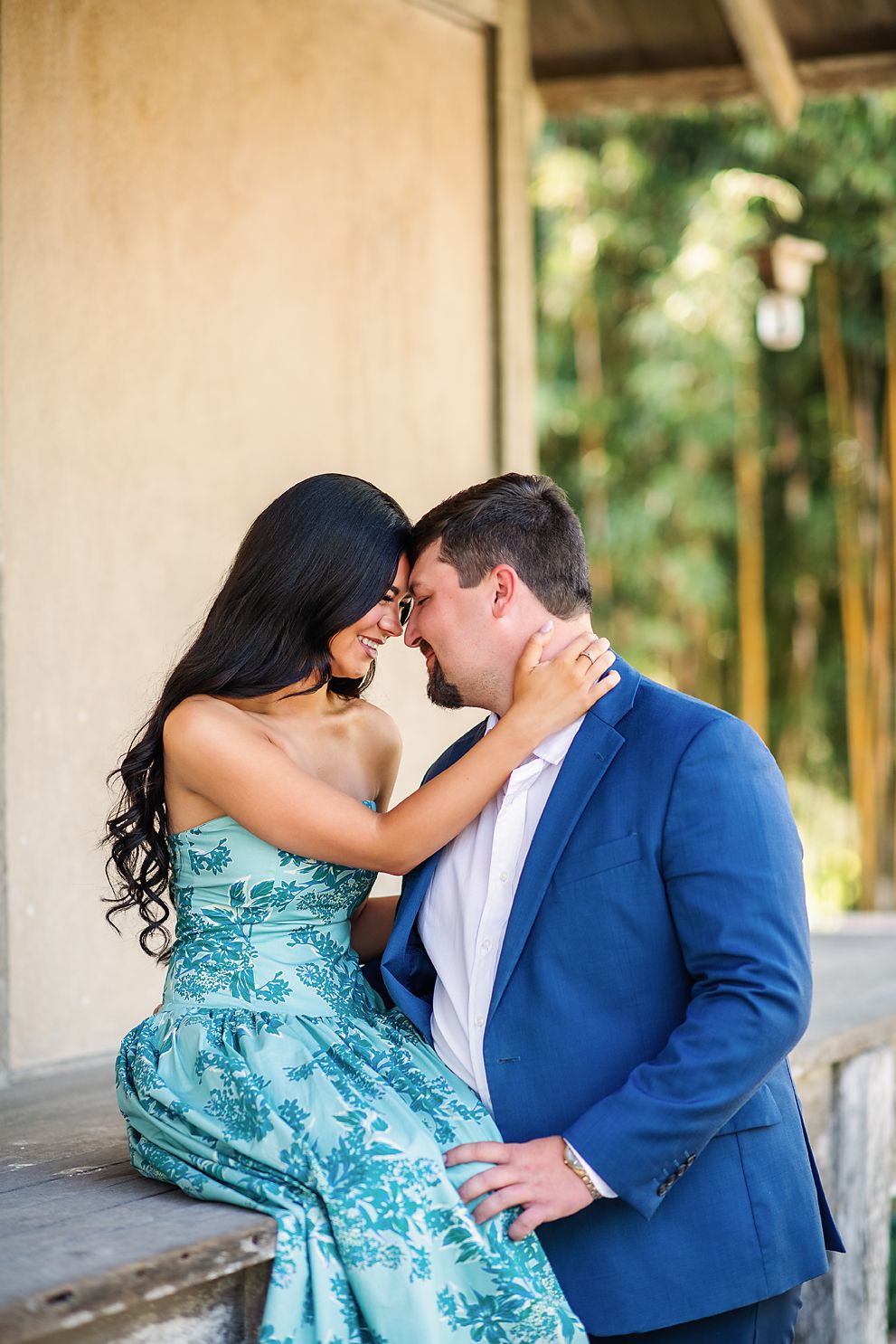 Couple in elegant attire sharing an intimate moment, woman in teal floral dress embracing man in blue suit.