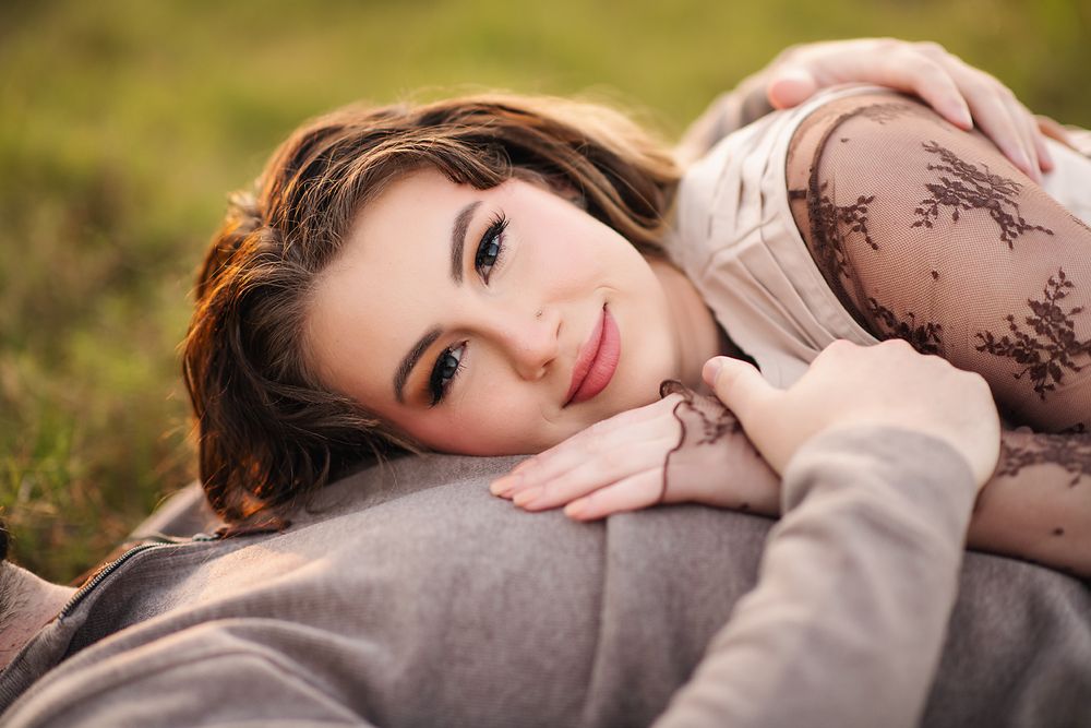 Young woman with brown hair smiling while lying on a lap outdoors in natural light.