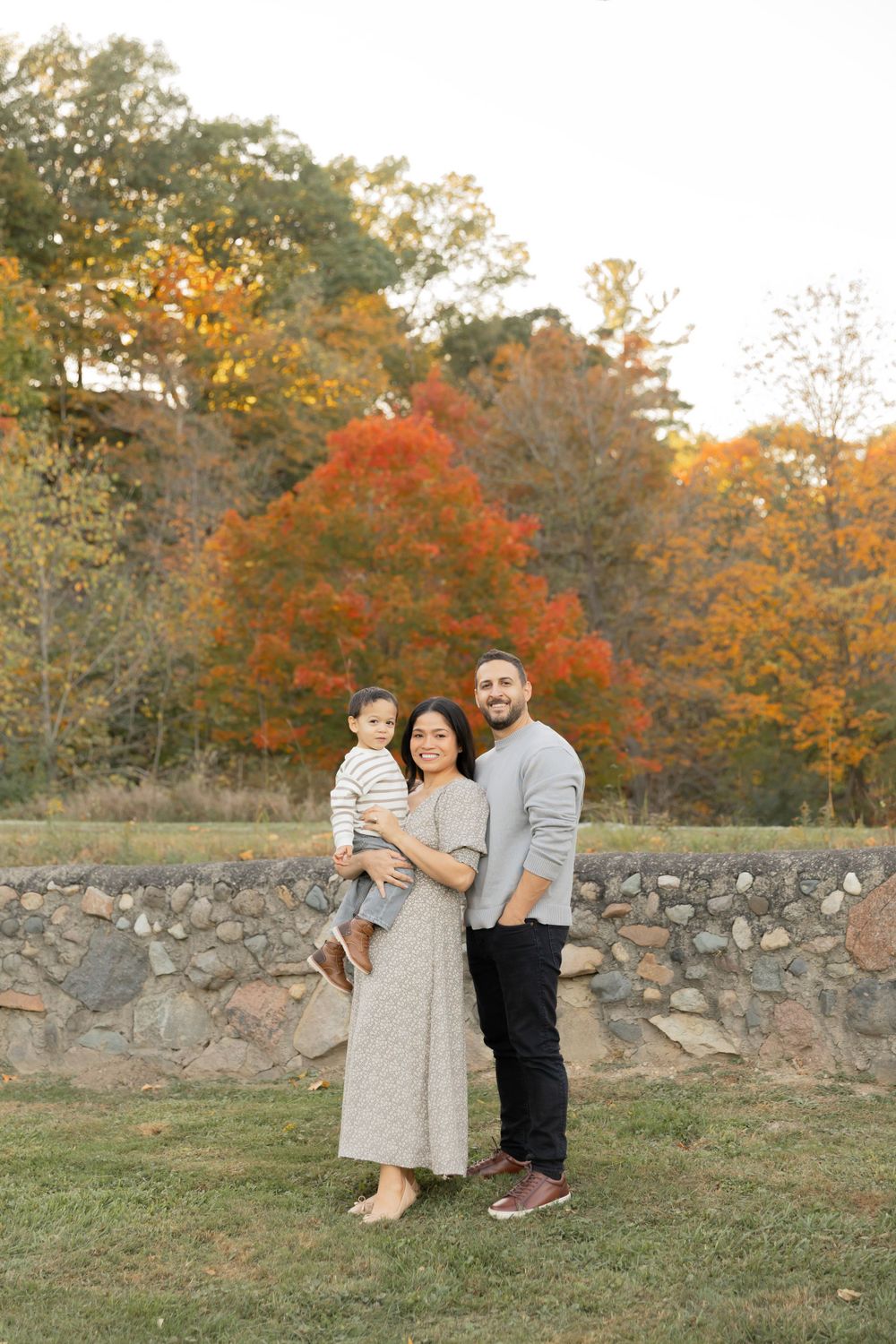 family holding their toddler standing in front of a historic brick wall in the fall in rochester michigan