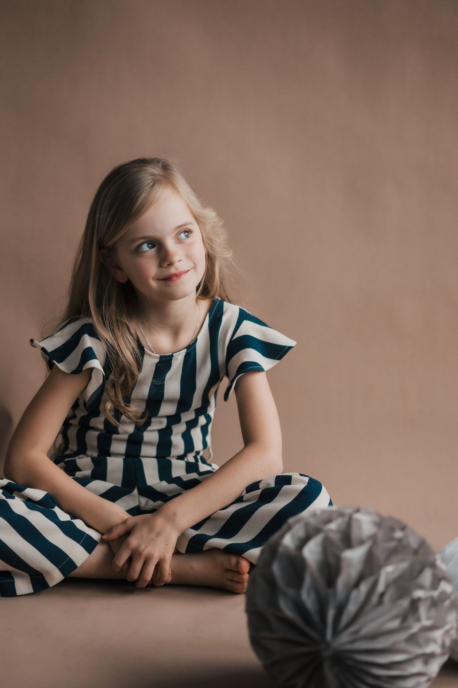 Child poses playfully in a striped dress against a brown backdrop in a studio portrait series.