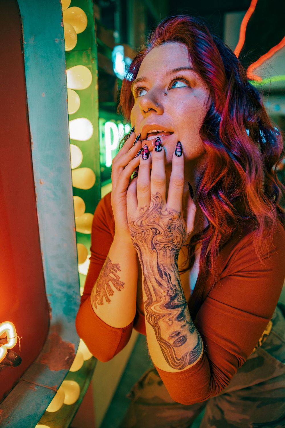 Series of artistic portraits showing a person with tattoos posing against a colorful neon sign background.