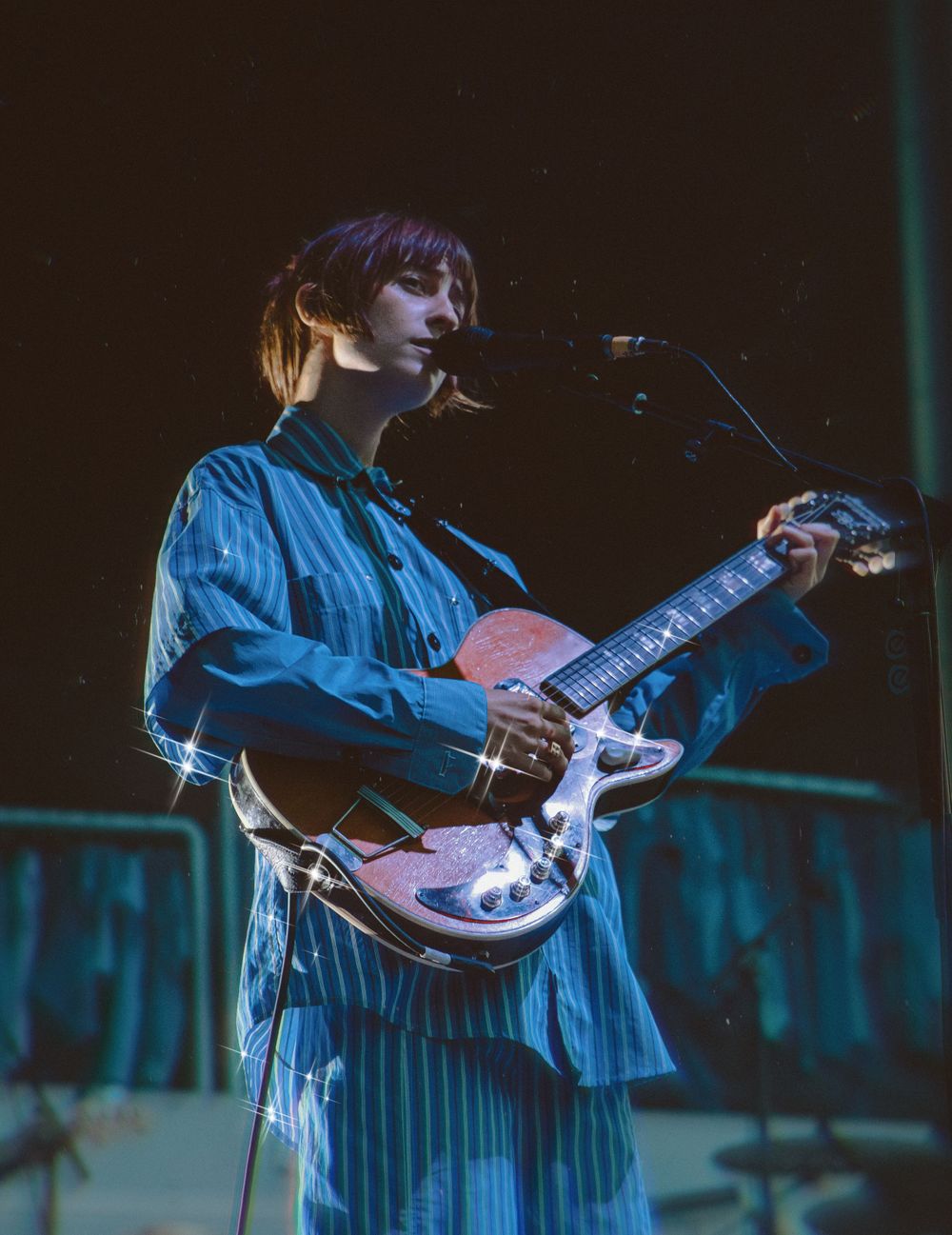 A musician performs on stage with a vintage guitar wearing a blue striped outfit under dramatic lighting.