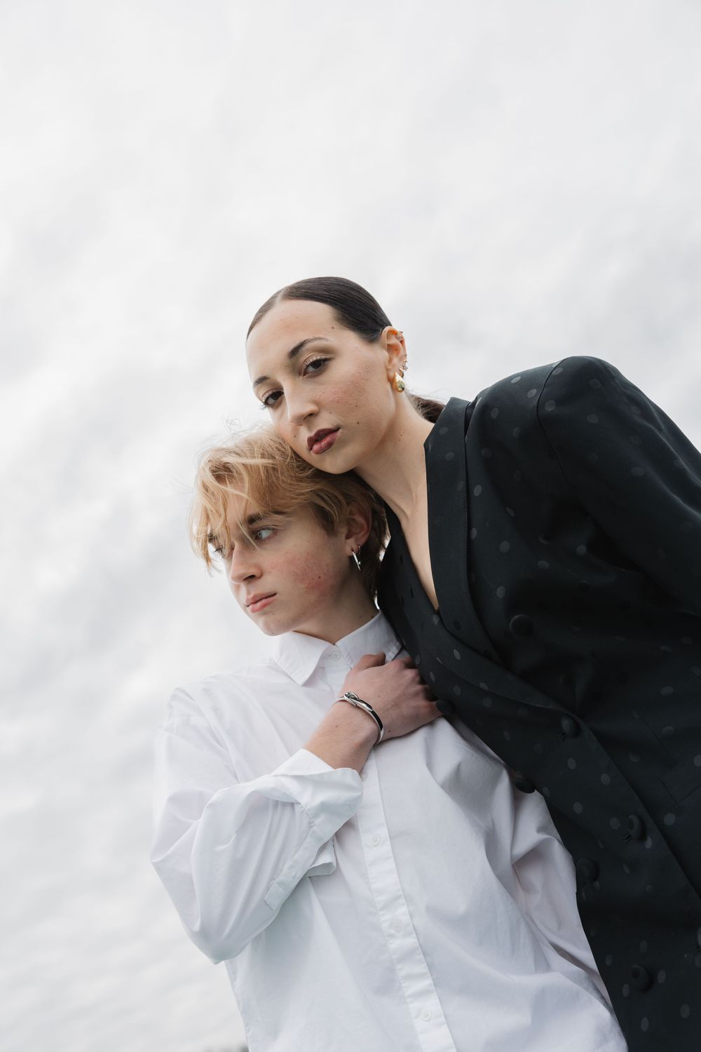 Two people in black and white outfits pose intimately against a light background in an artistic fashion portrait series.