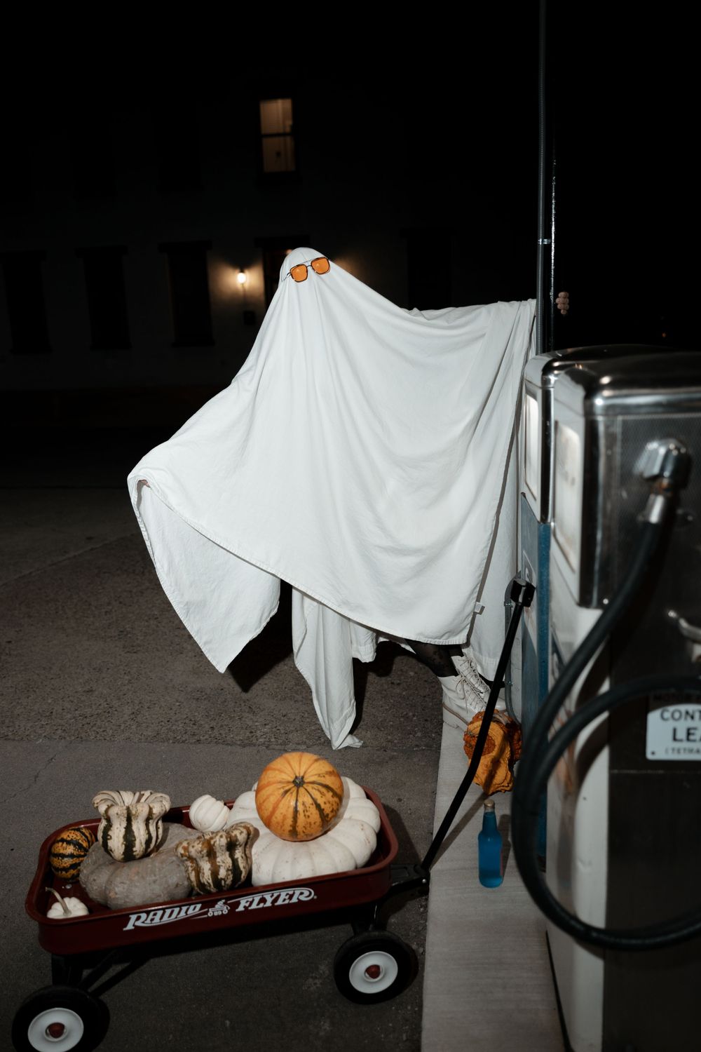 A Halloween ghost decoration made from white fabric draped over a wagon with pumpkins and fall decor underneath.