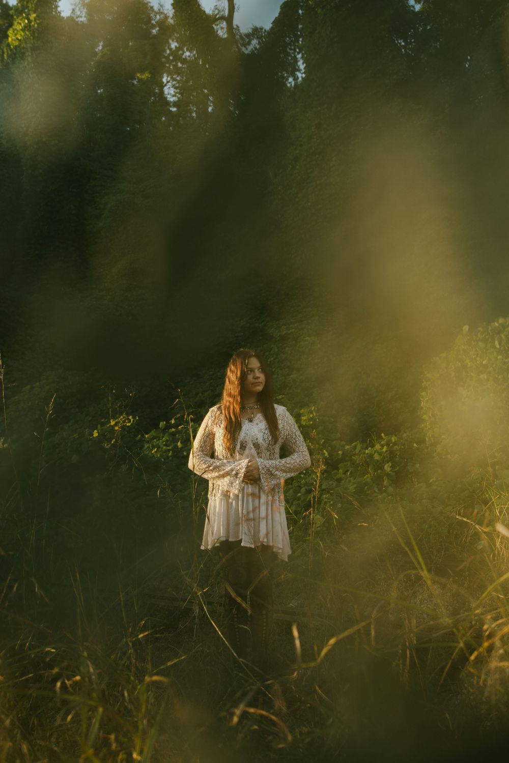 Dreamy outdoor portrait session in a meadow with golden sunlight filtering through trees and tall grass.