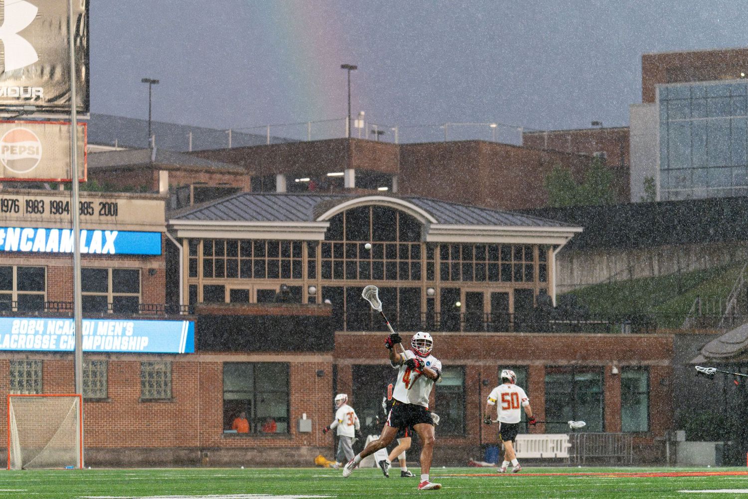 Soccer players practicing on field with buildings visible in background.