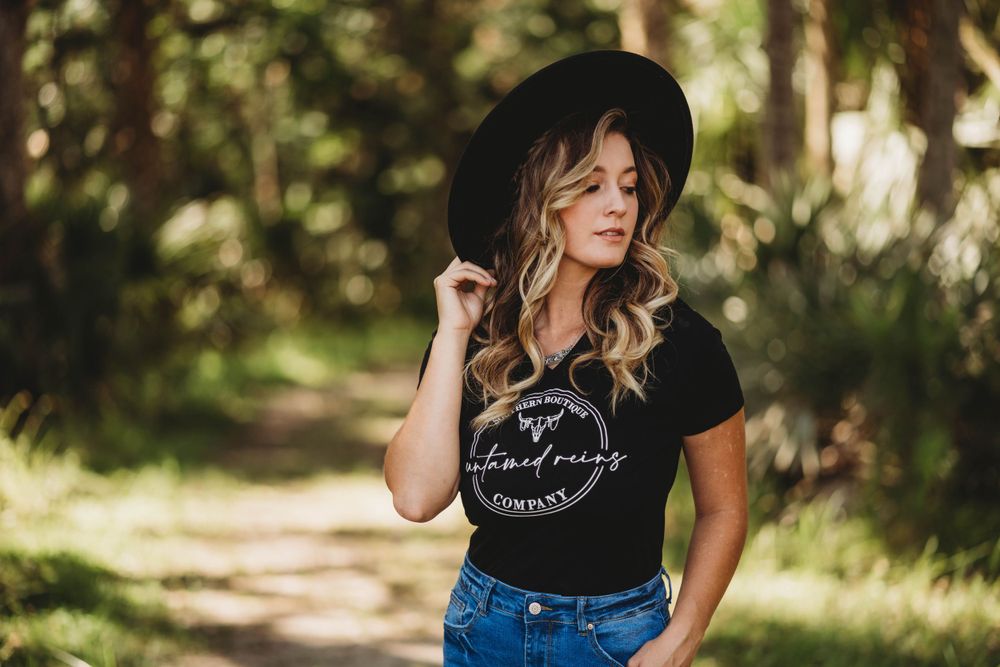 Casual western style with black t-shirt, jeans and wide-brim hat in natural forest setting.