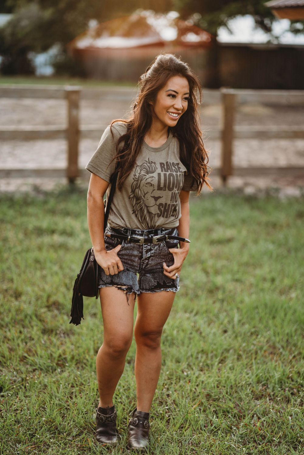 Casual summer outfit featuring graphic tee, denim shorts and boots in rustic outdoor setting.