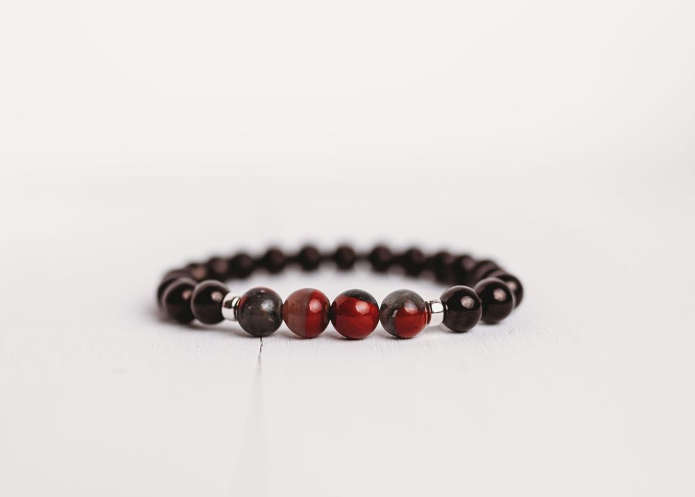 Beaded bracelet with dark and red stones on white background.