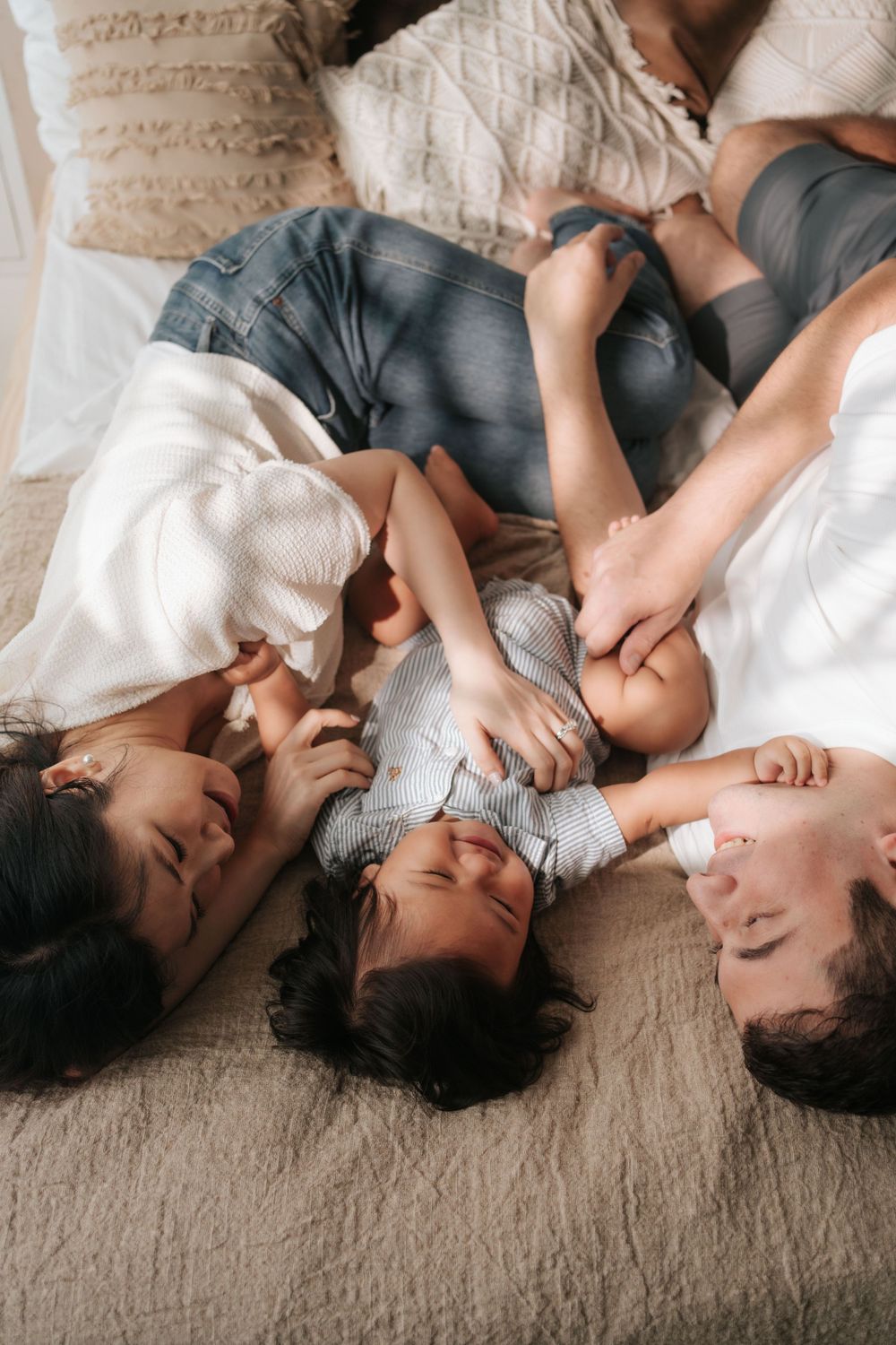 Family lying together on beige carpet in casual attire.