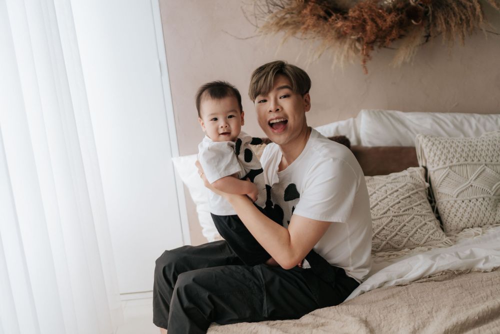 Joyful parent holding smiling baby while sitting together on comfortable couch.