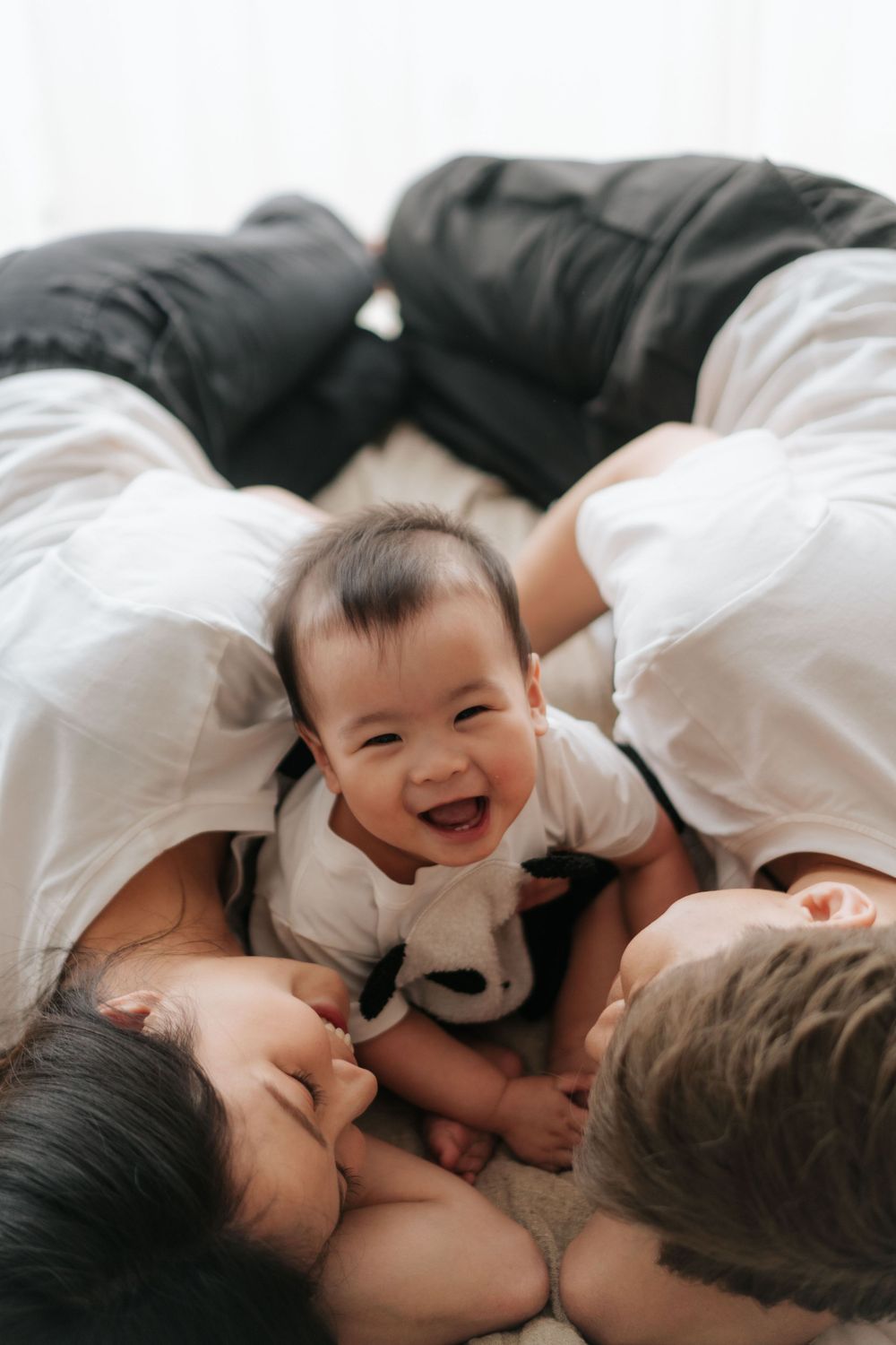 Joyful family cuddle session on white bedding.