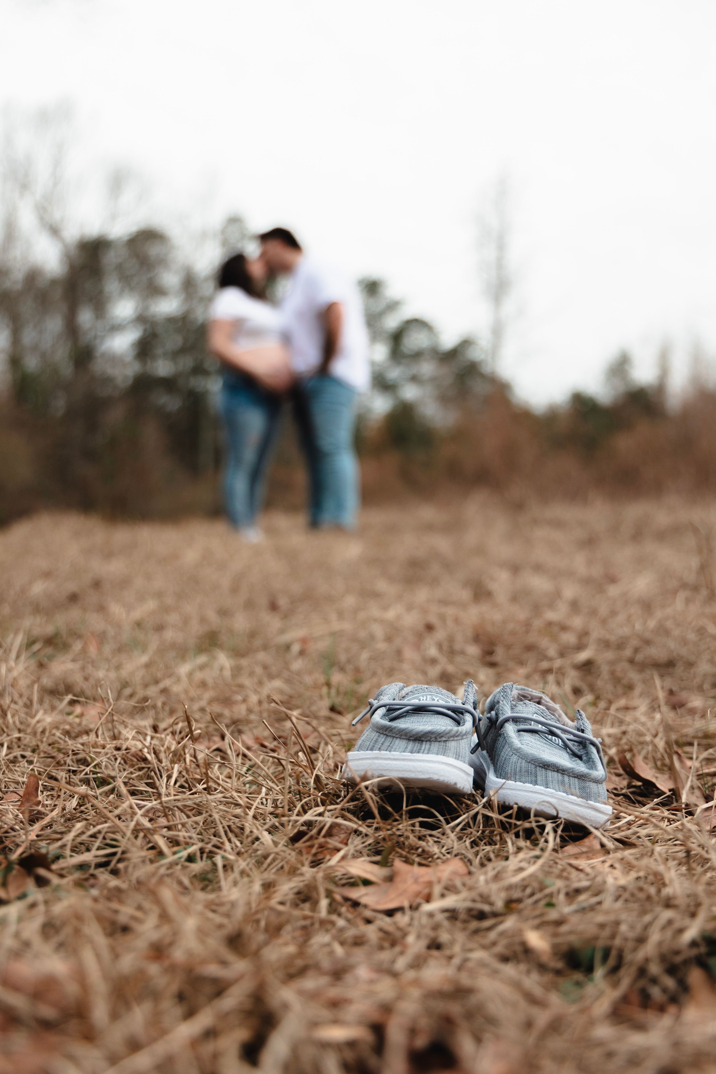 Small baby shoes placed on dried grass with blurred figures in the background.