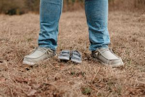 Close-up view of legs wearing jeans and sneakers standing on brown grass.