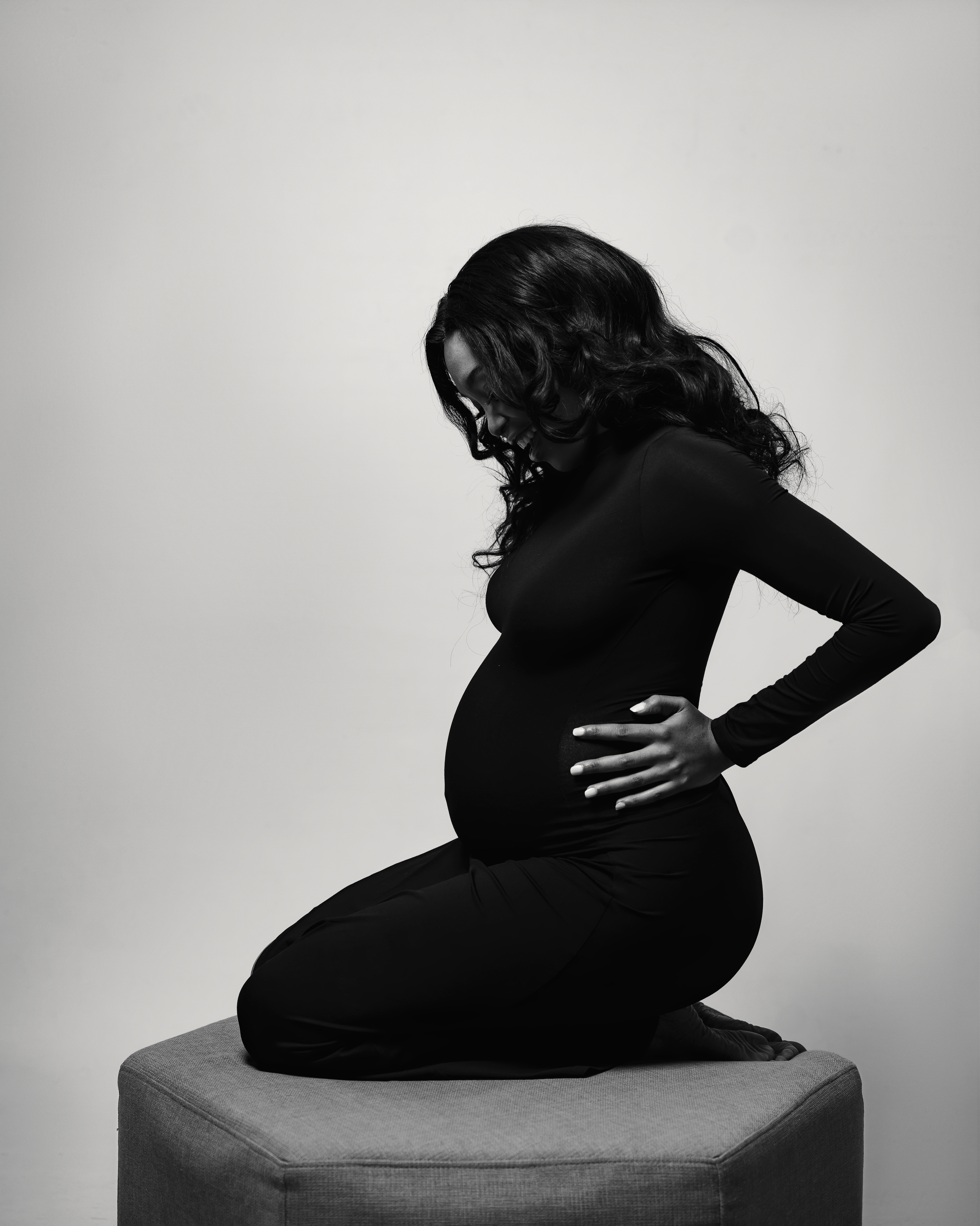 Dramatic black and white maternity photo with expectant mother posed on geometric pedestal.