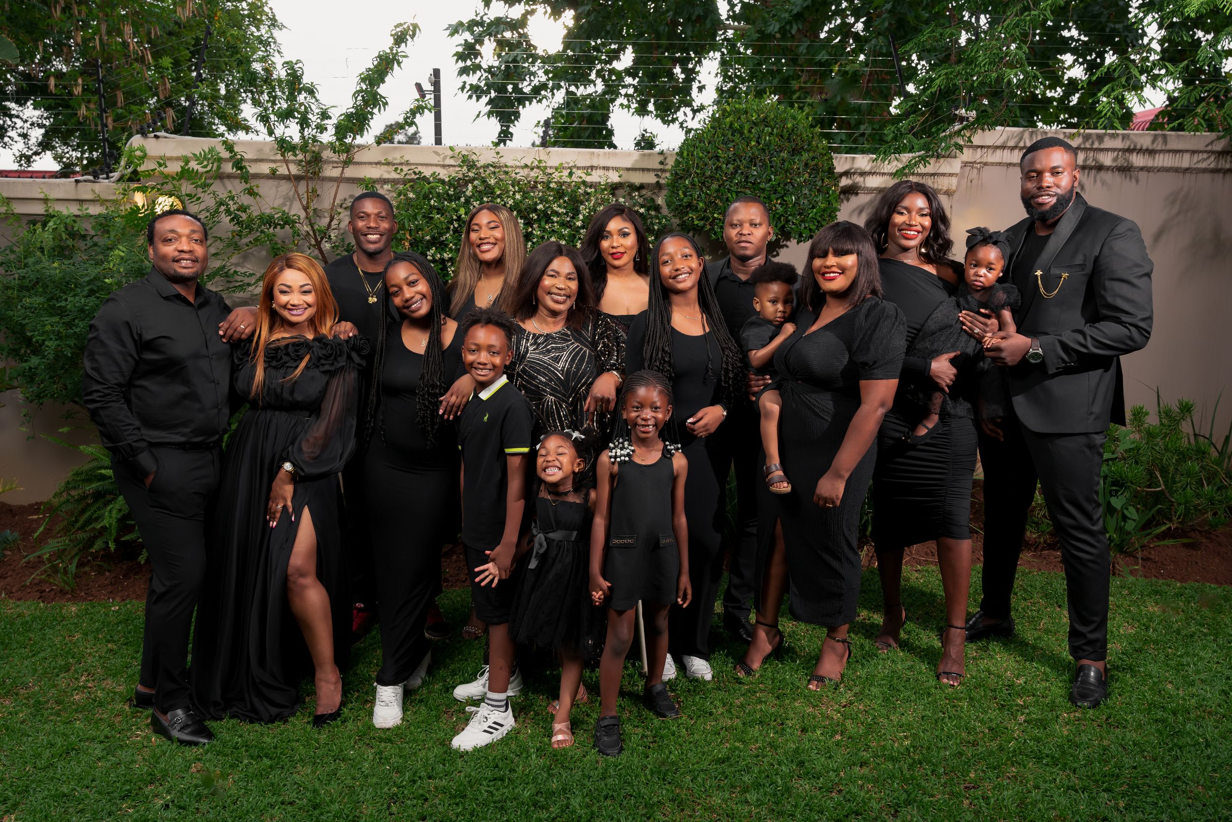 Large family group photo with all members wearing coordinated black formal attire in garden setting.