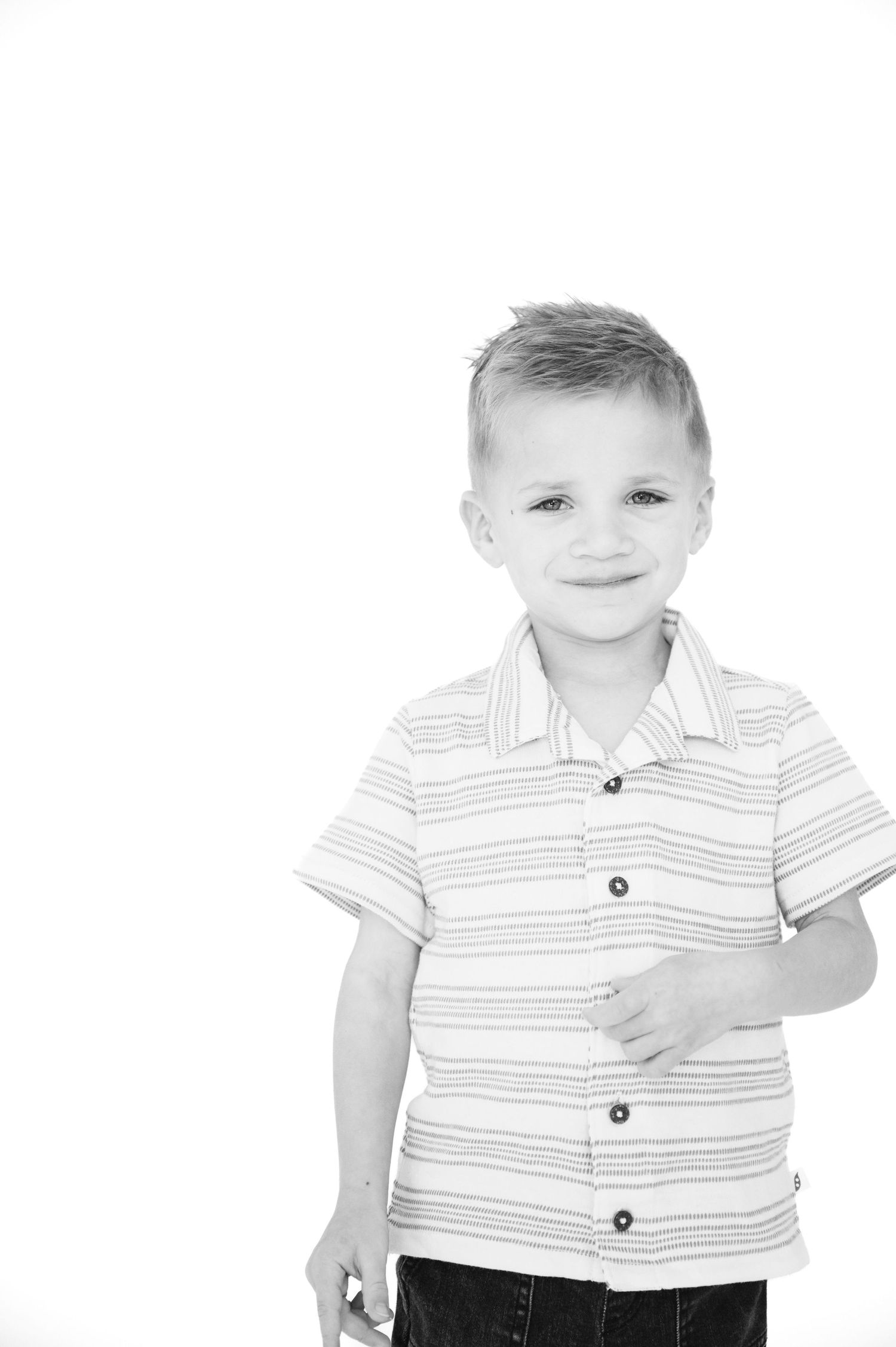 Black and white studio portrait of a young boy wearing striped polo shirt against white background.