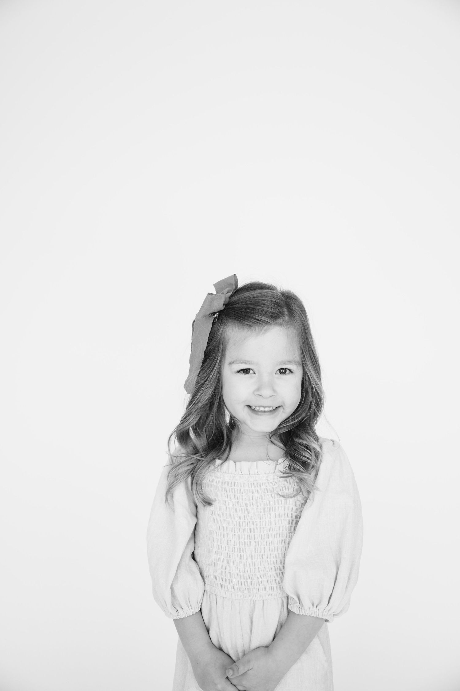 Black and white portrait of a young girl in a smocked dress with bow hair accessory.