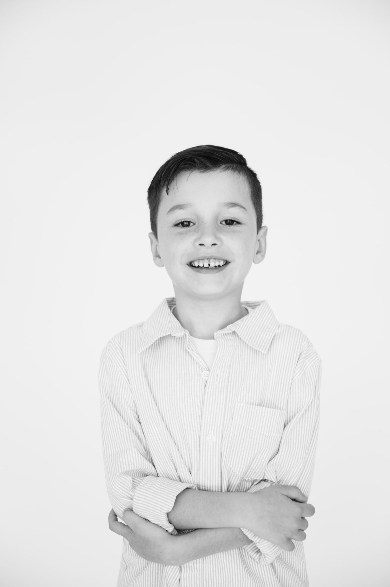 Black and white studio portrait of a boy in striped shirt with arms crossed.