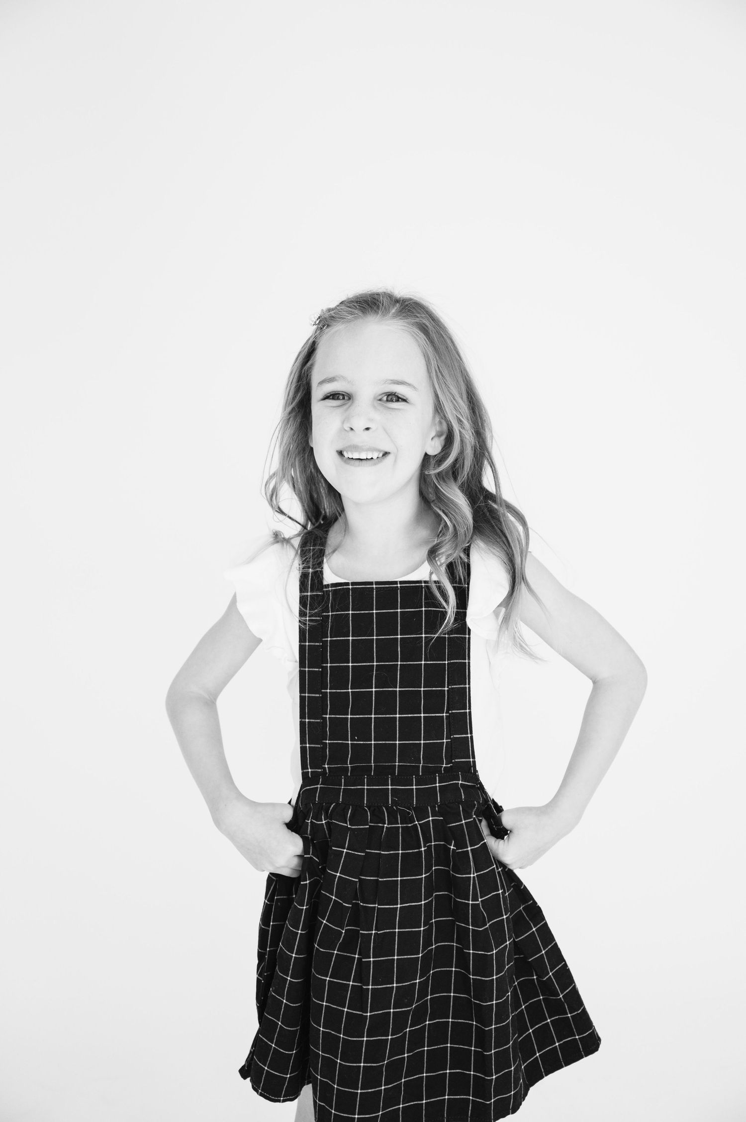 Young person in black and white checkered dress poses with hands on hips against white background.