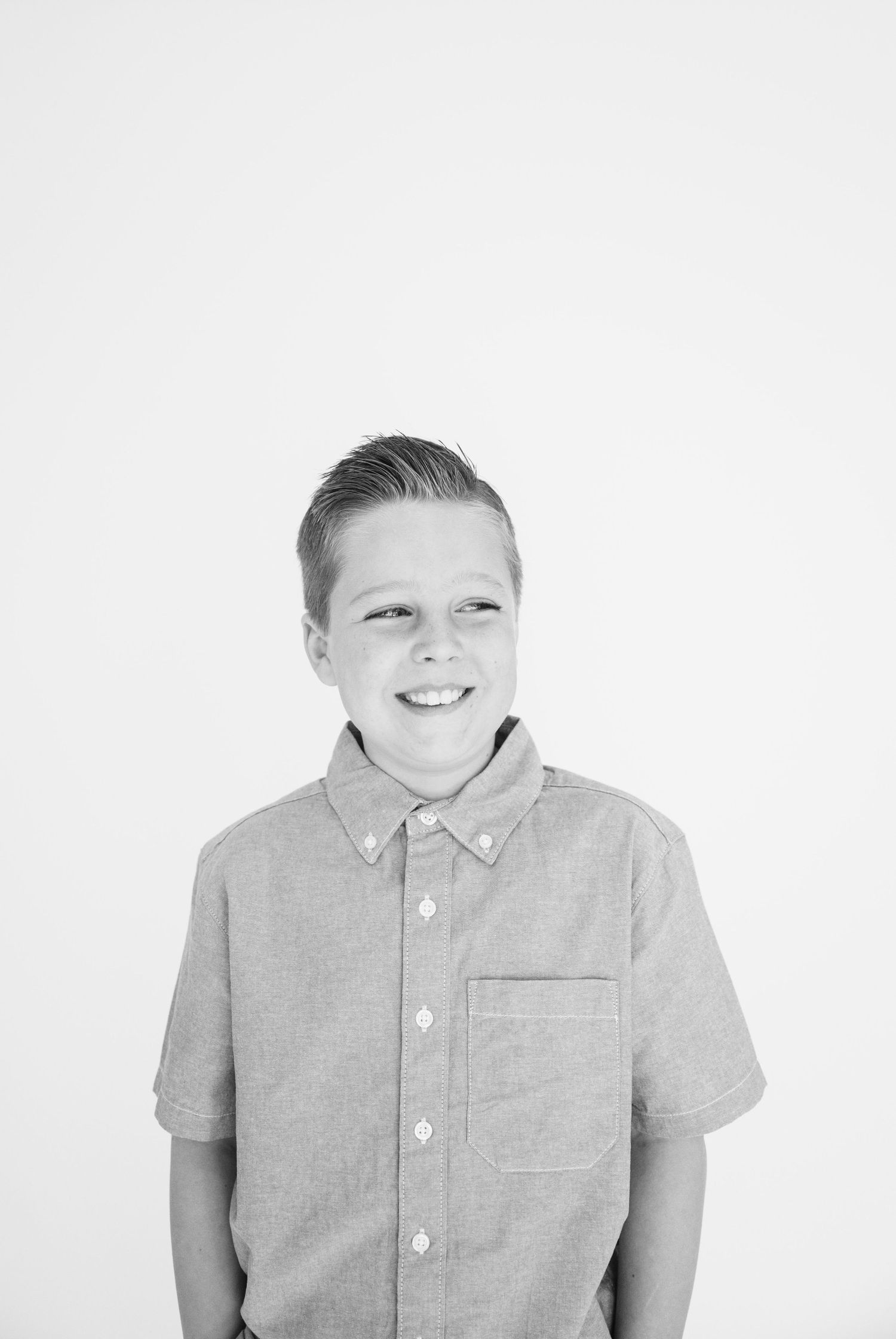 Portrait of young person in collared short sleeve shirt smiling at camera against white backdrop.