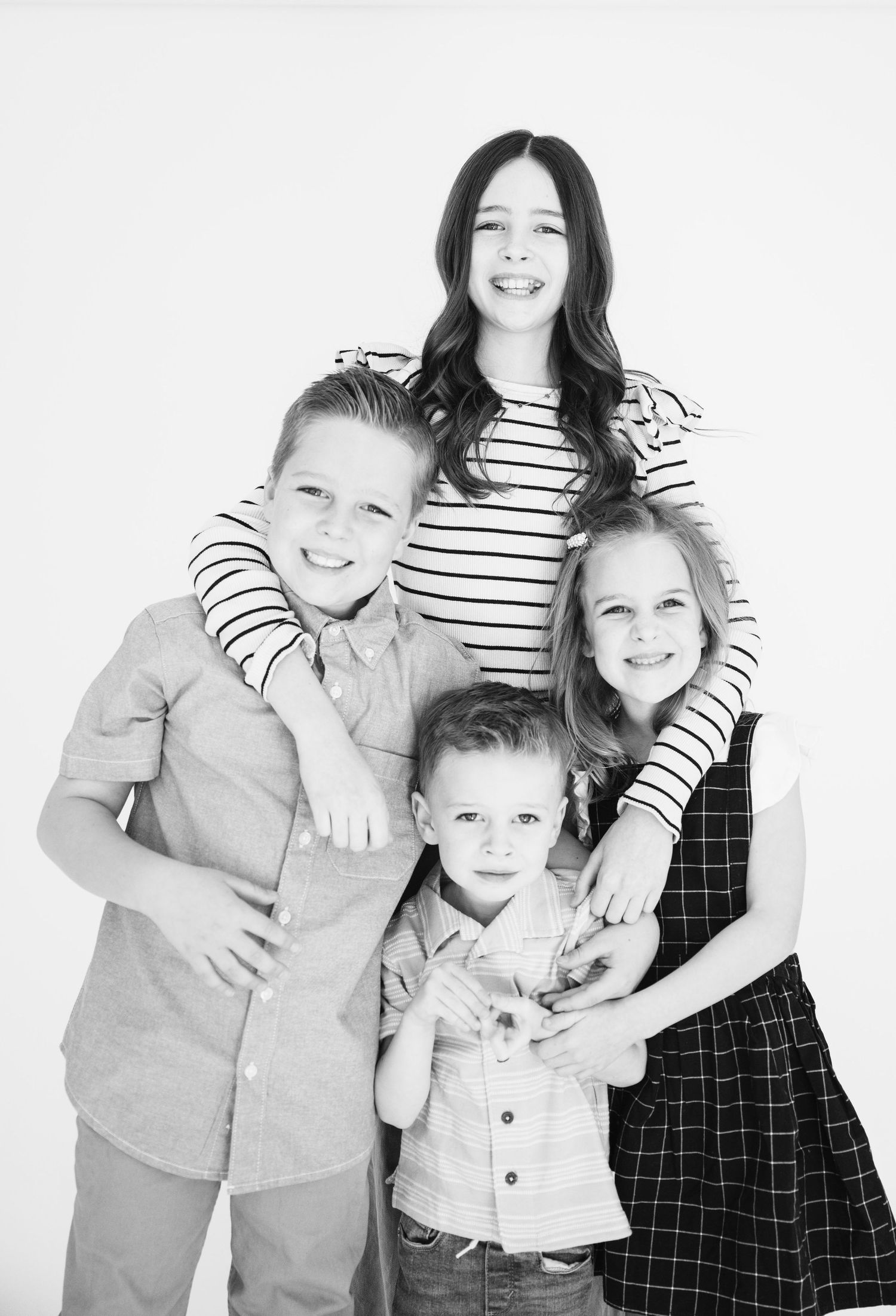 Black and white family portrait of four siblings in casual attire against white background.