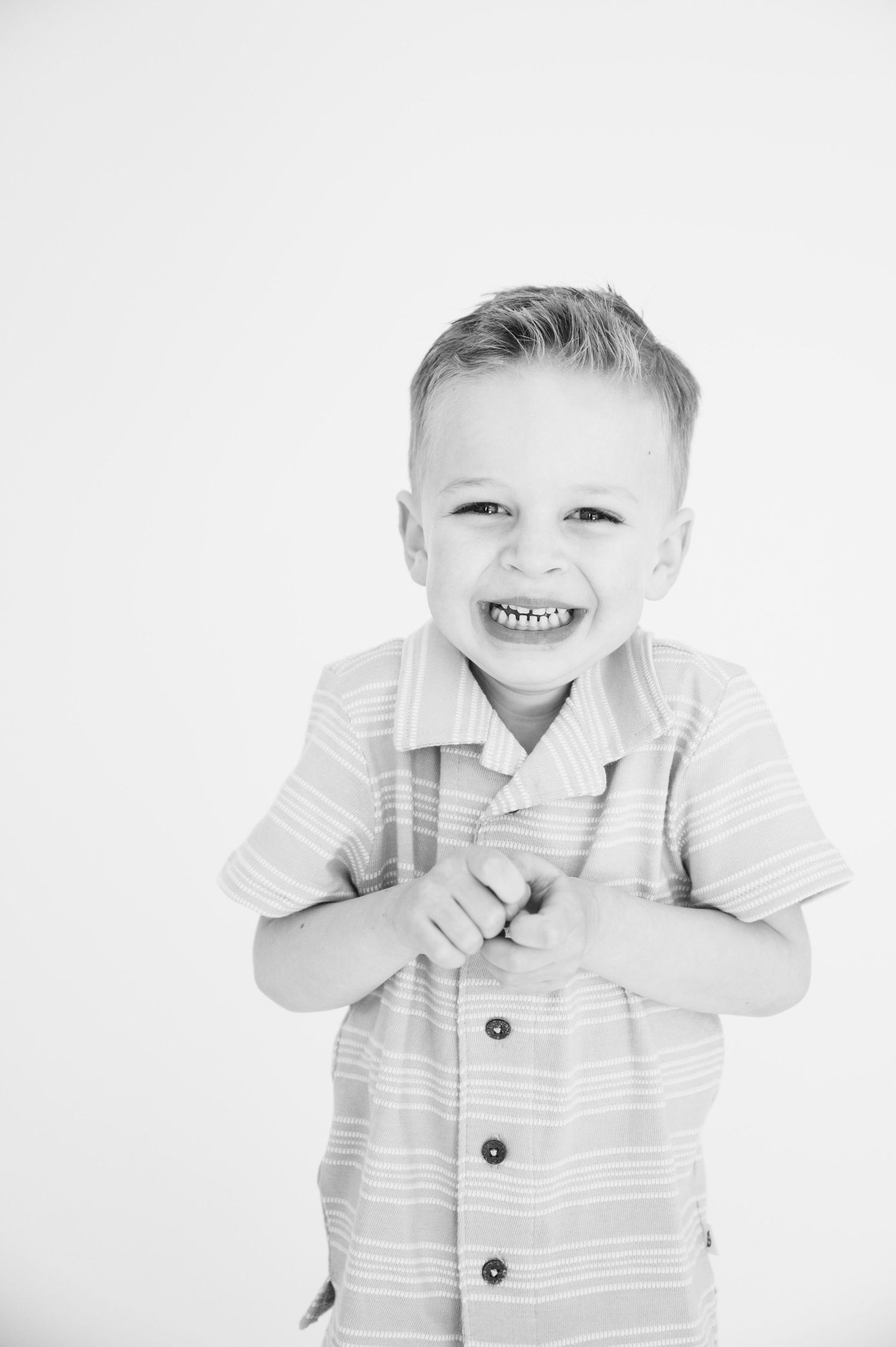 Close up black and white portrait of young child smiling in striped button-up shirt.