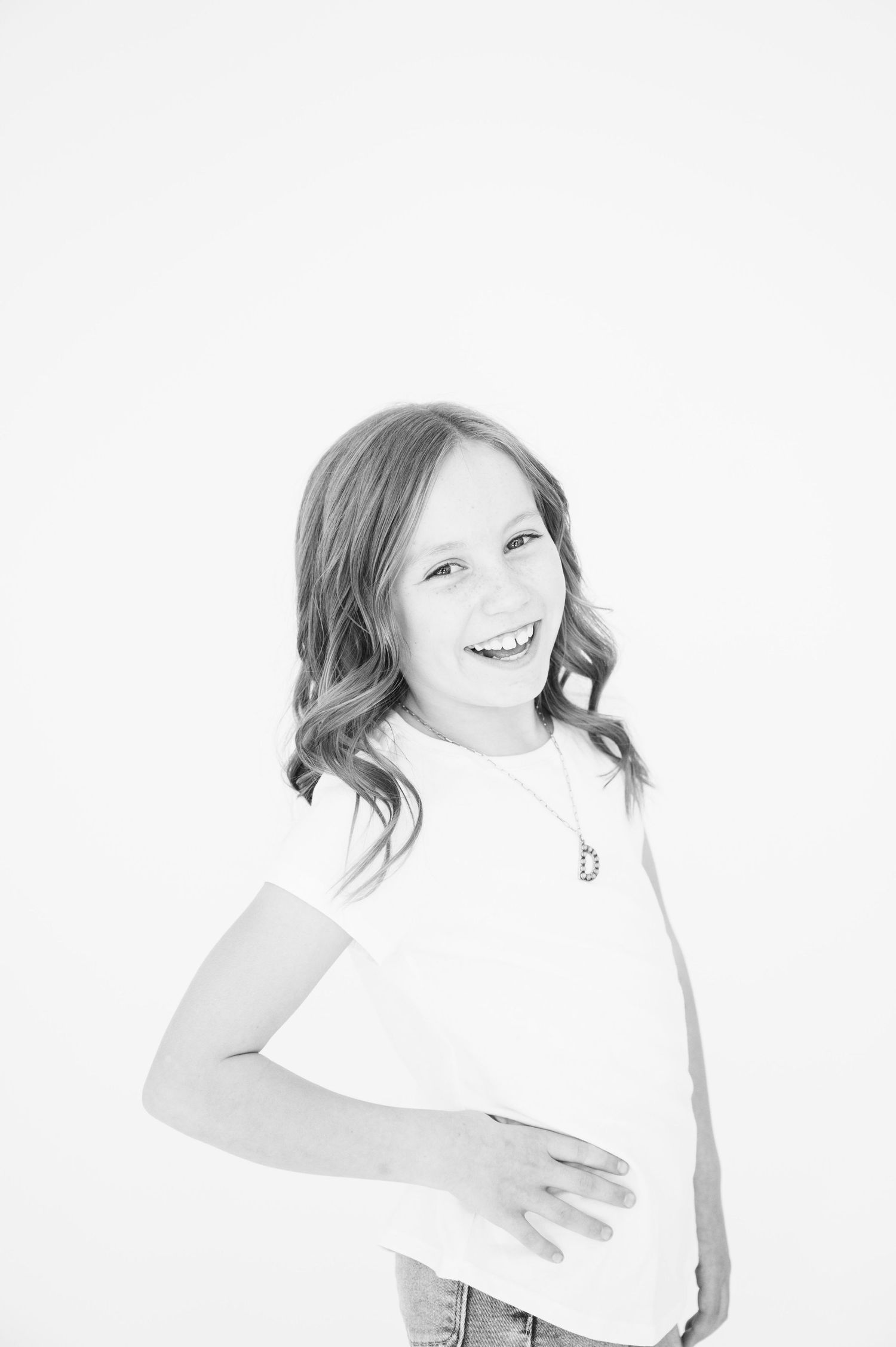Black and white portrait of person in white top with wavy hair posing against white background.