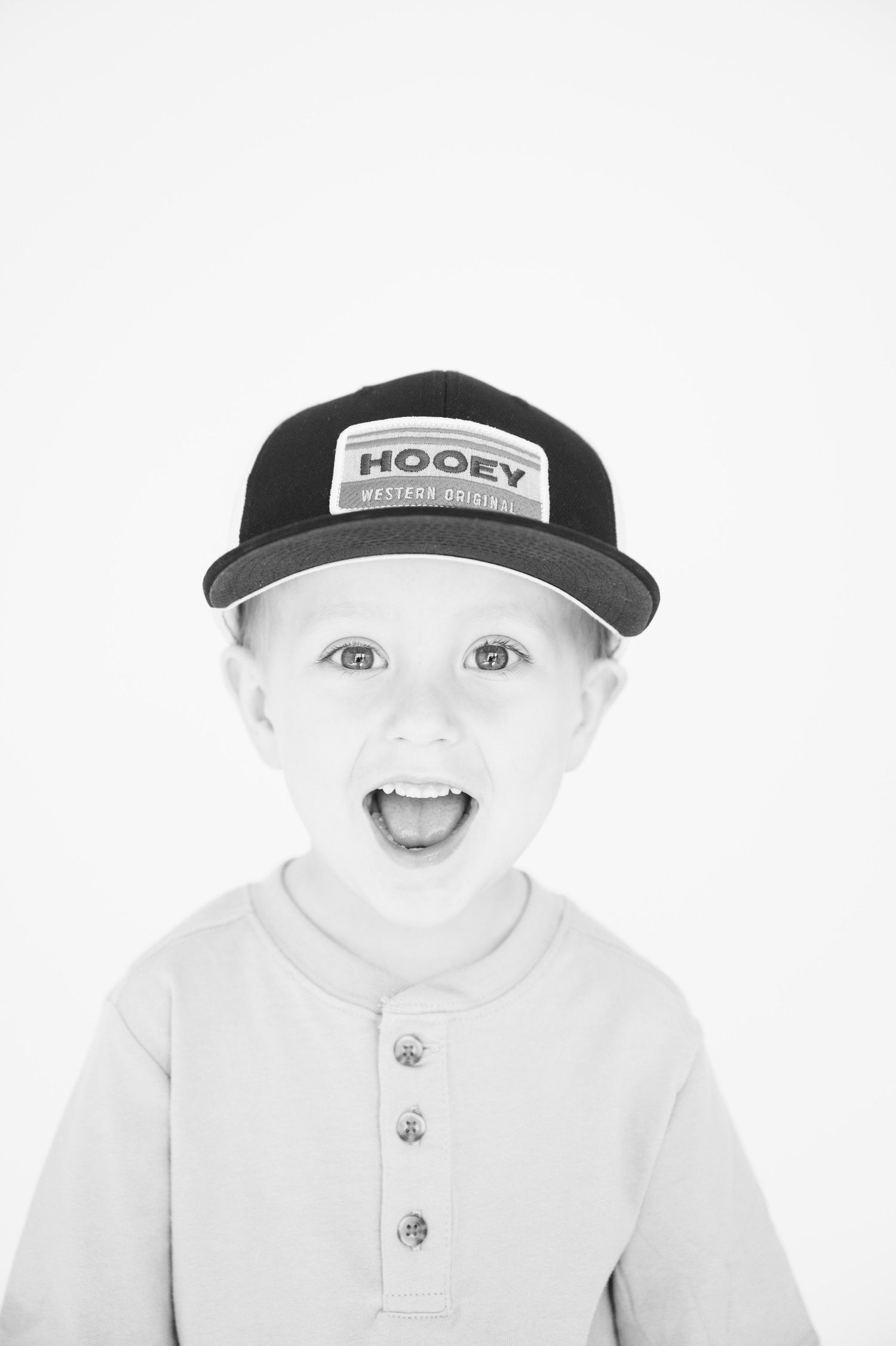 Young person wearing Hooey branded baseball cap smiling enthusiastically at camera.