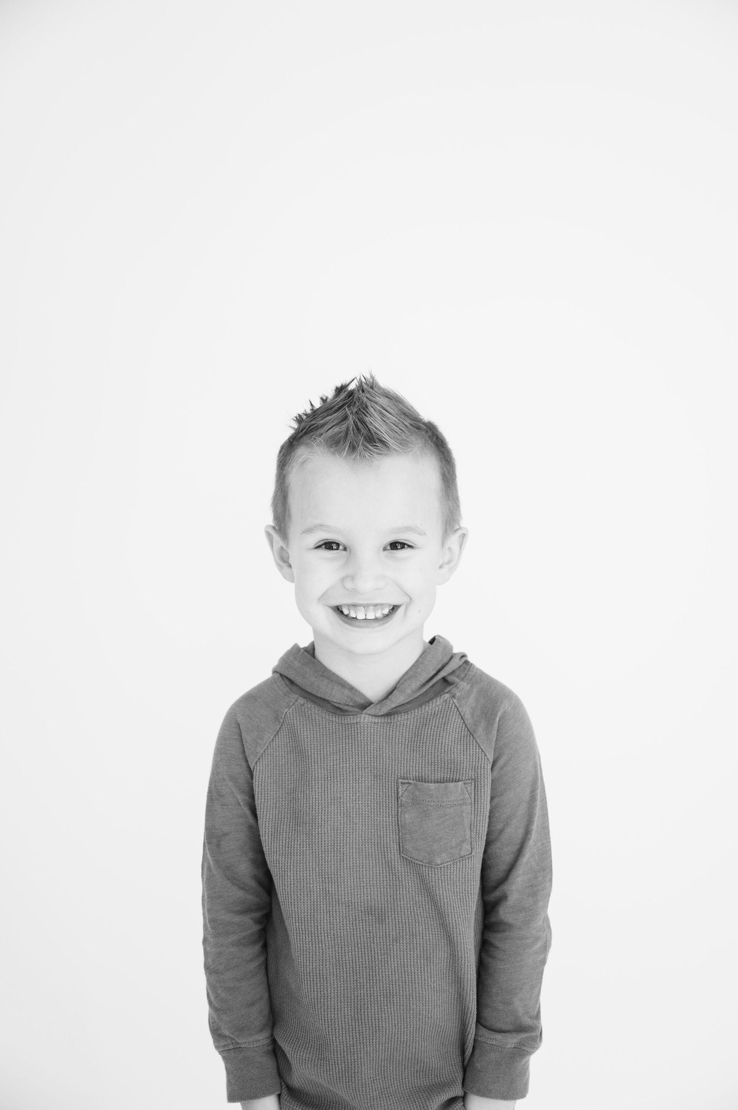 Black and white portrait of young child in hooded sweater against white backdrop.
