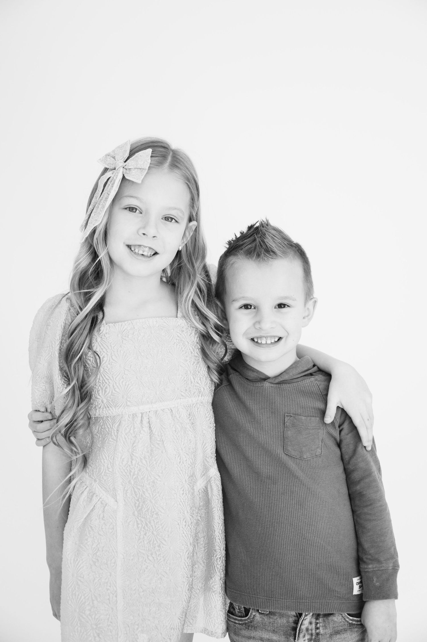 Black and white studio portrait of two children in casual attire against white background.