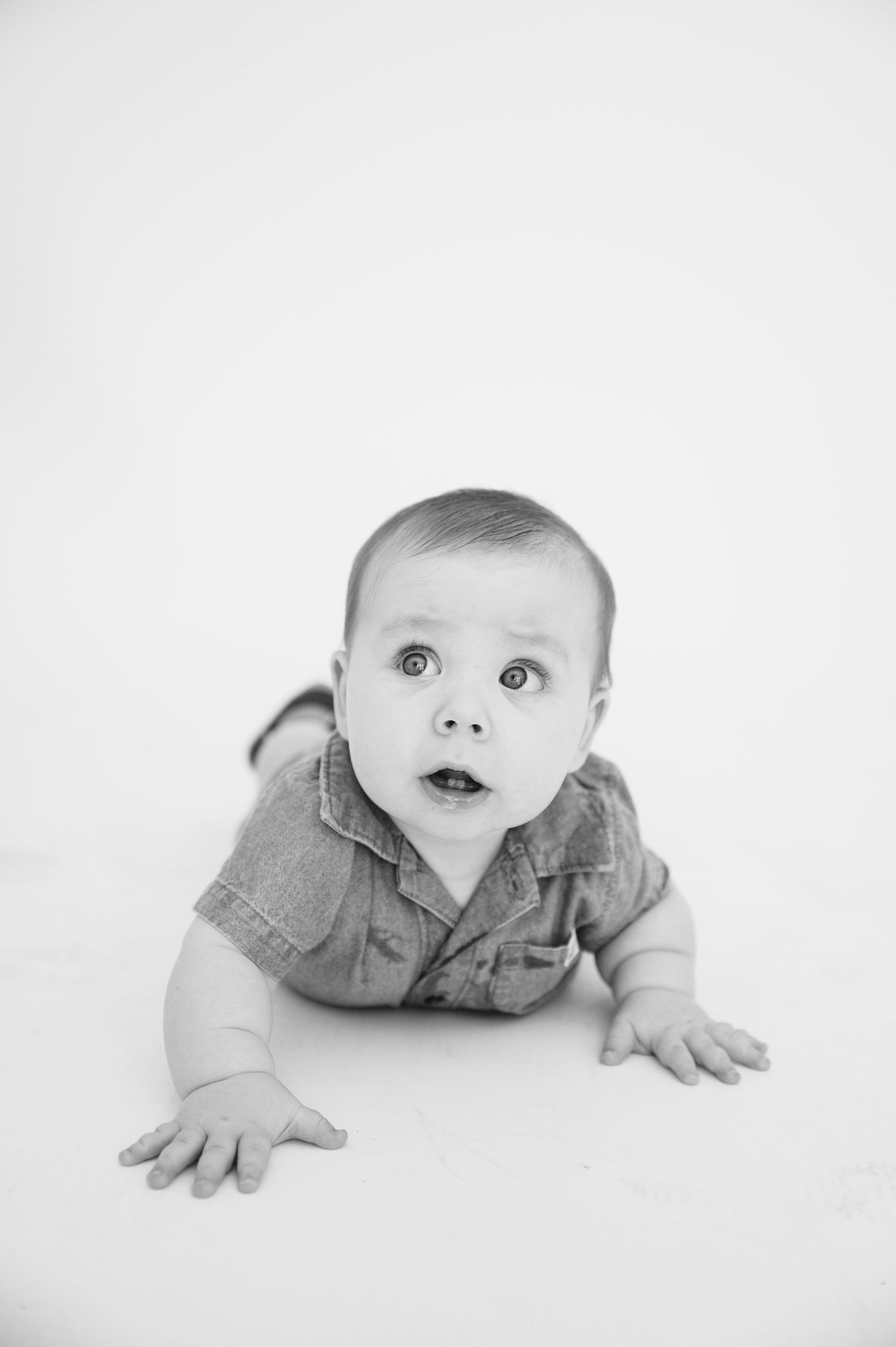 Black and white photo of infant in denim crawling on white background.