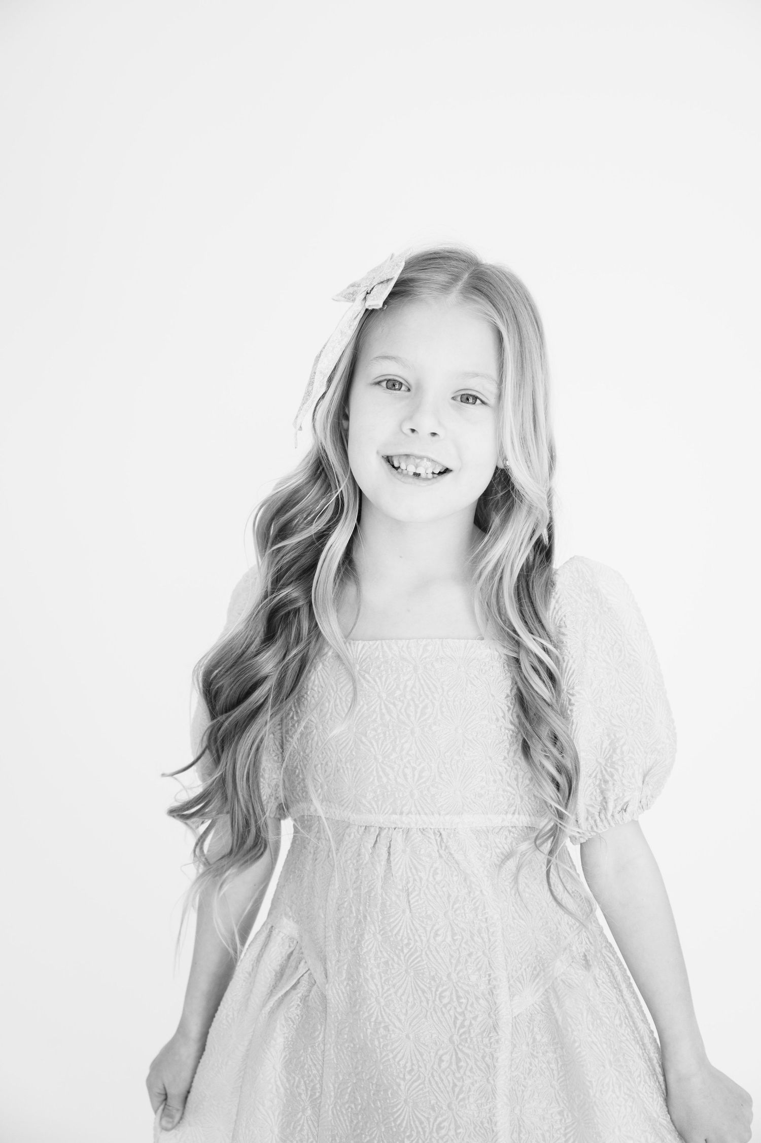 Portrait of young person with long wavy hair wearing puff sleeve dress against white background.