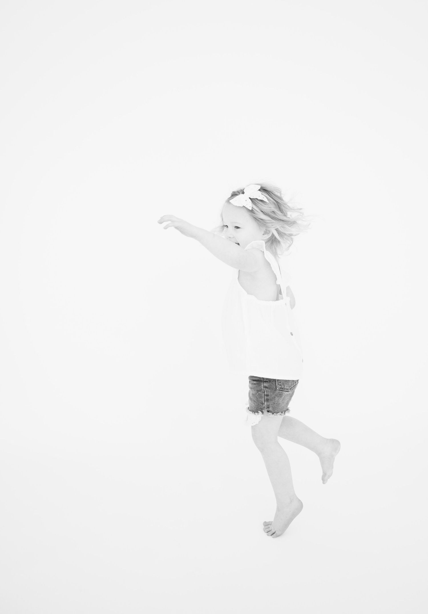 Black and white image of child jumping with arms outstretched against white background.