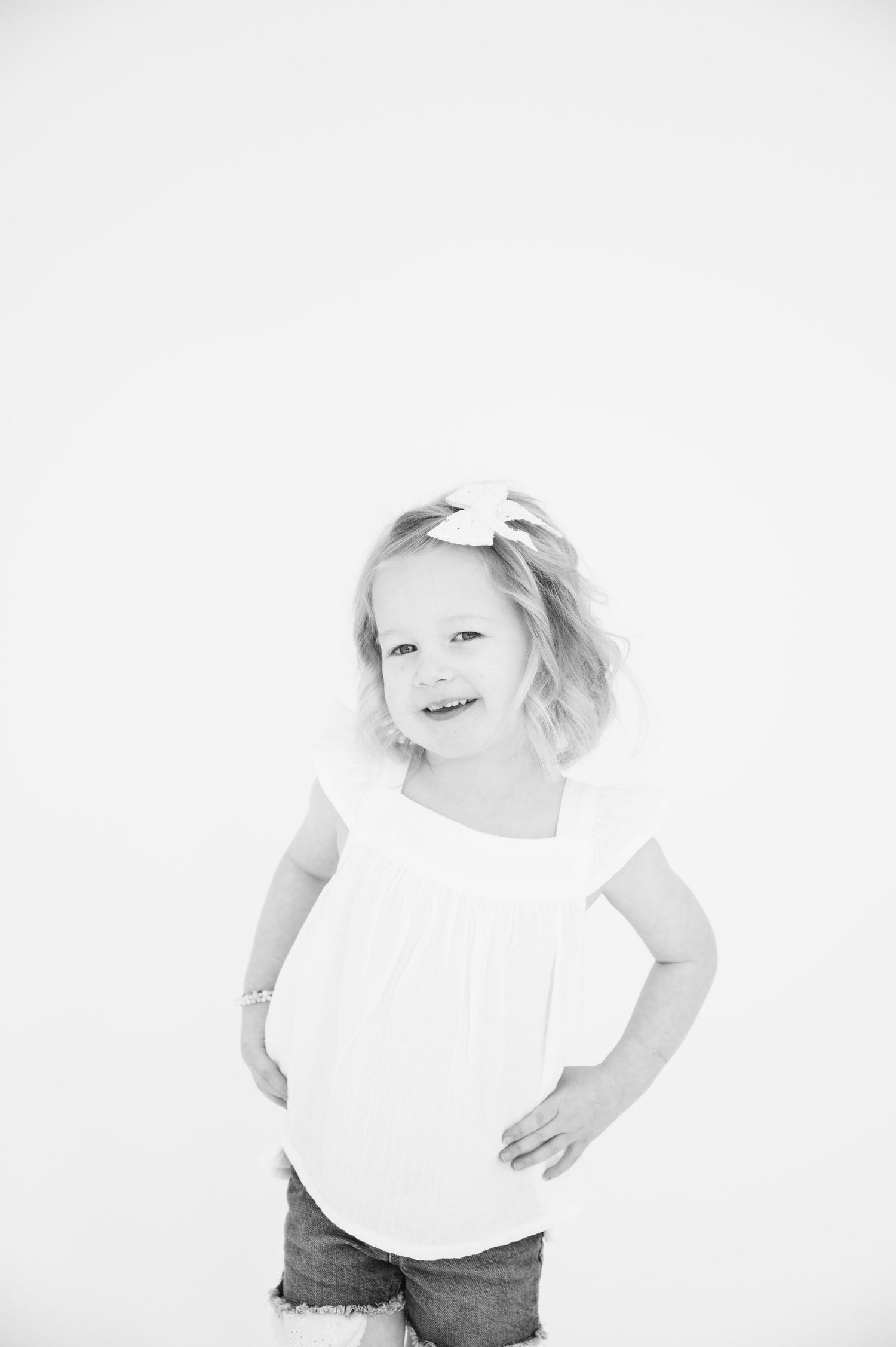Black and white portrait of child in summer outfit posing with hands on hips.