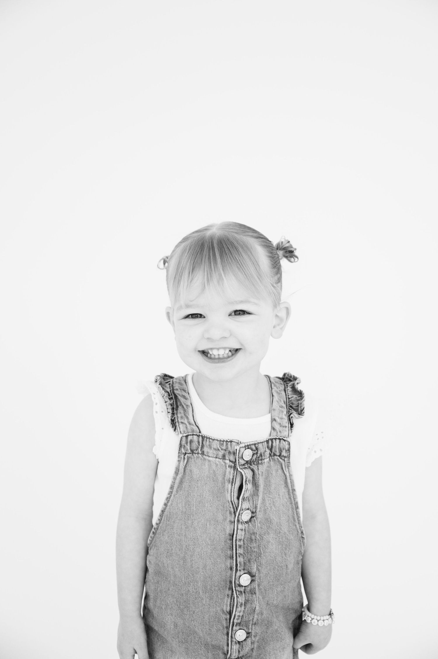 Black and white portrait of child wearing denim overalls with bright expression.