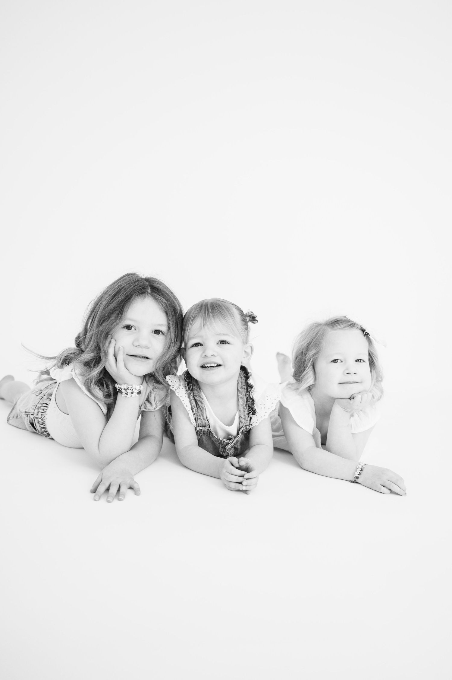 Black and white studio photo of three children lying together on white background.