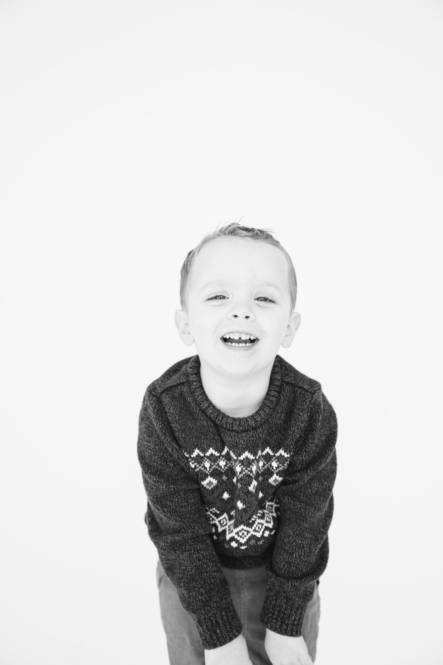 Black and white portrait of child wearing patterned winter sweater with joyful expression.