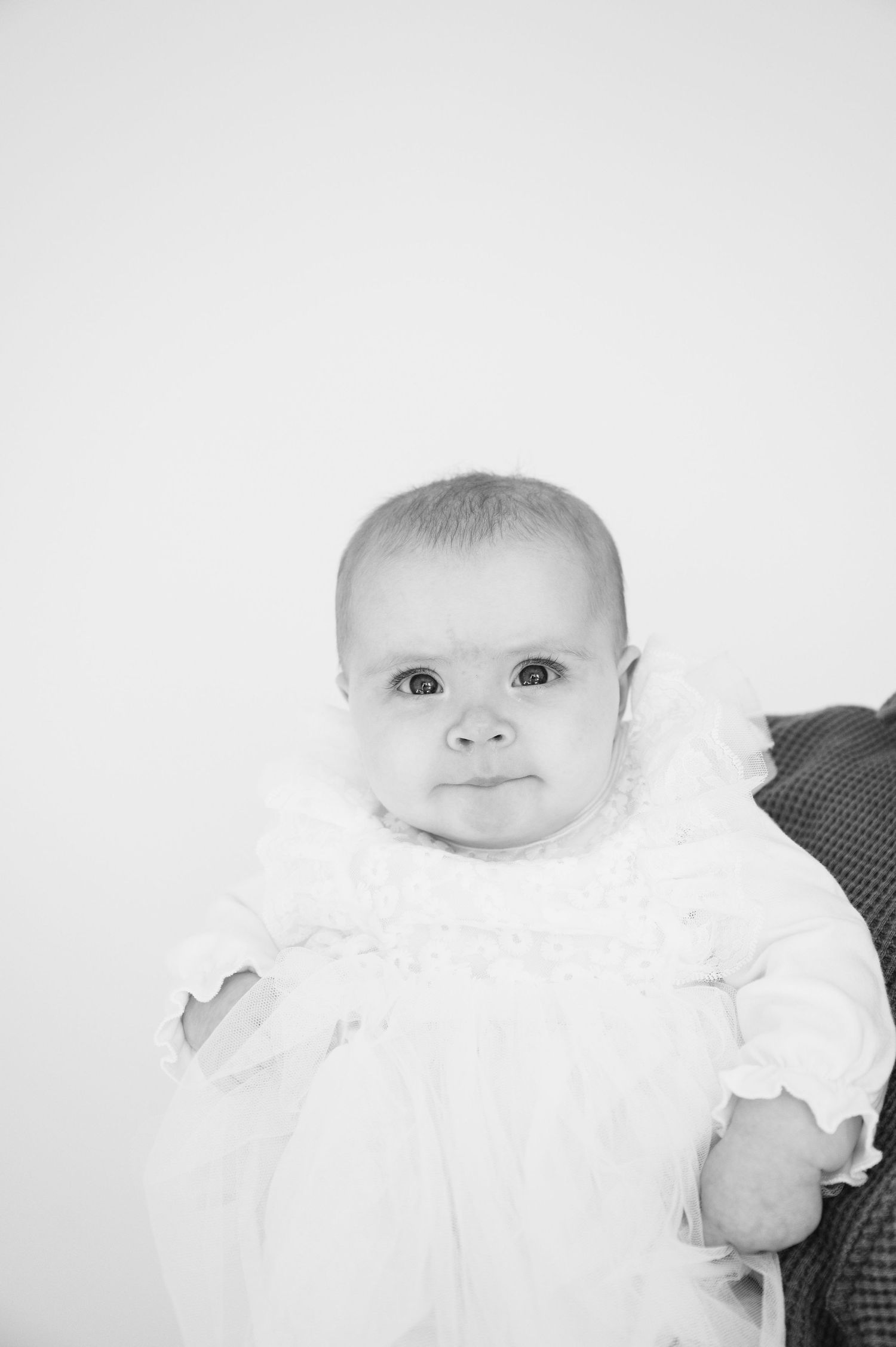 Black and white portrait of baby in white dress against light background.