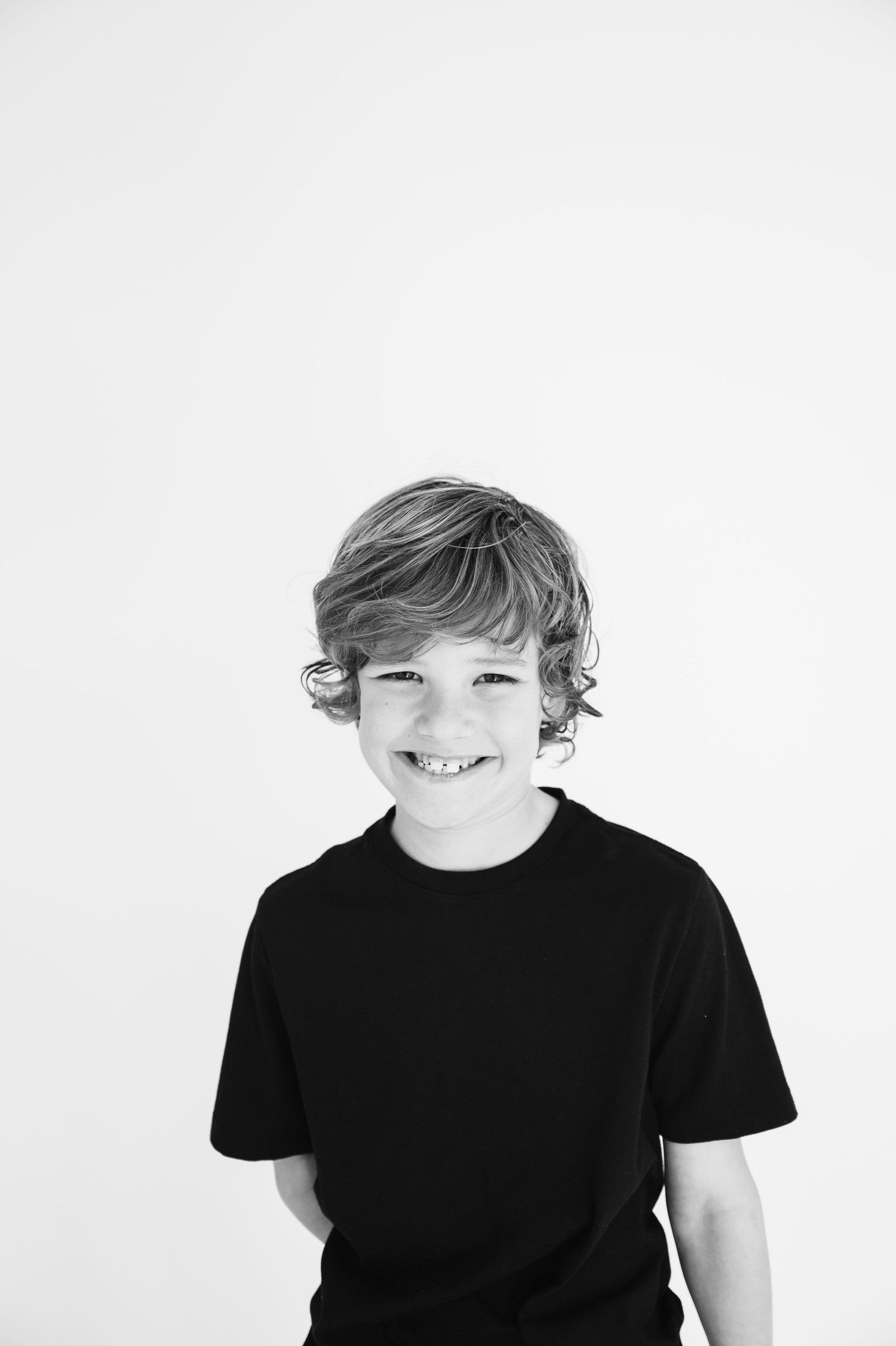 Black and white portrait of smiling child in dark t-shirt against white background.