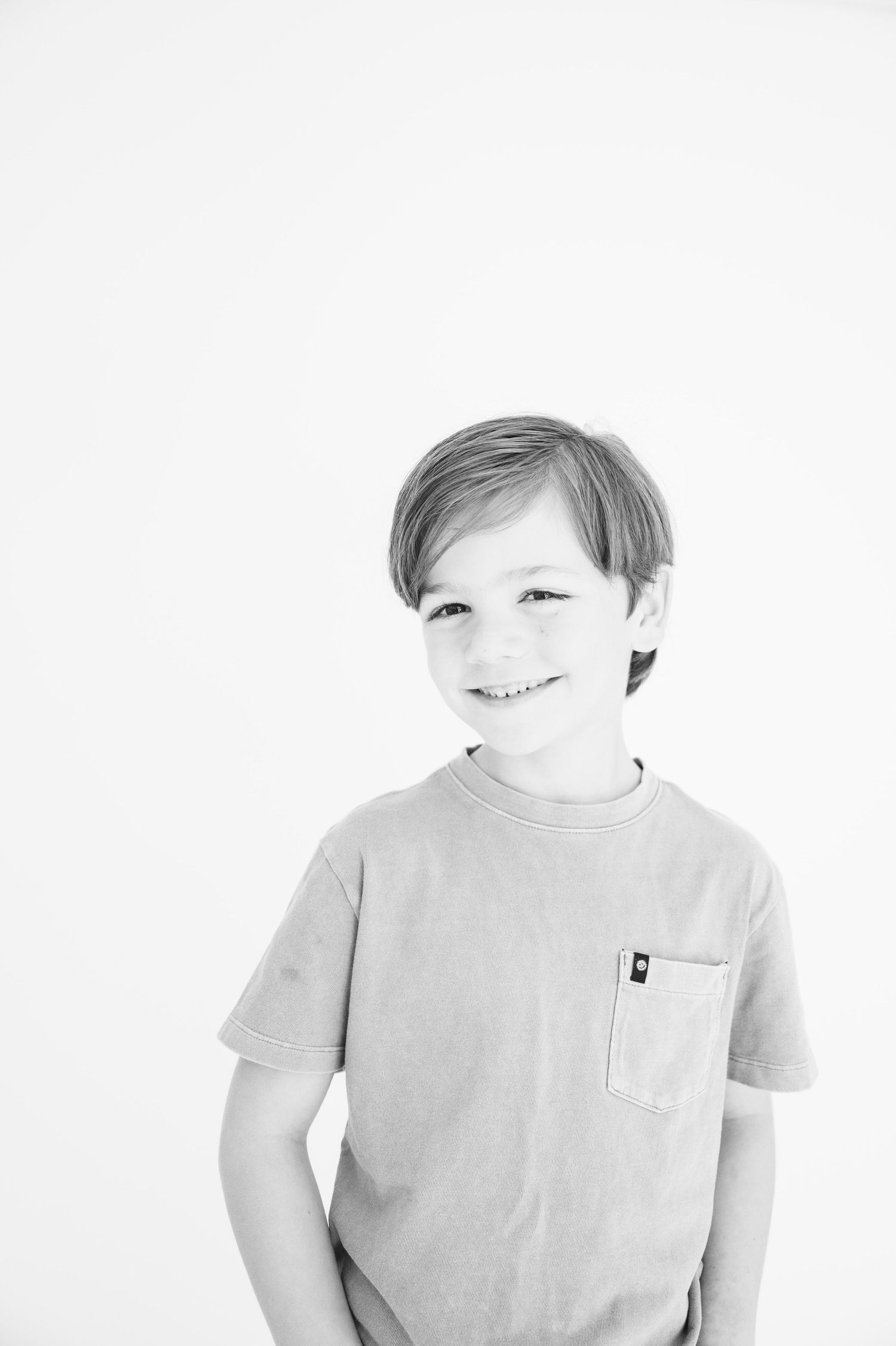 Black and white studio portrait of child wearing light colored t-shirt with pocket.