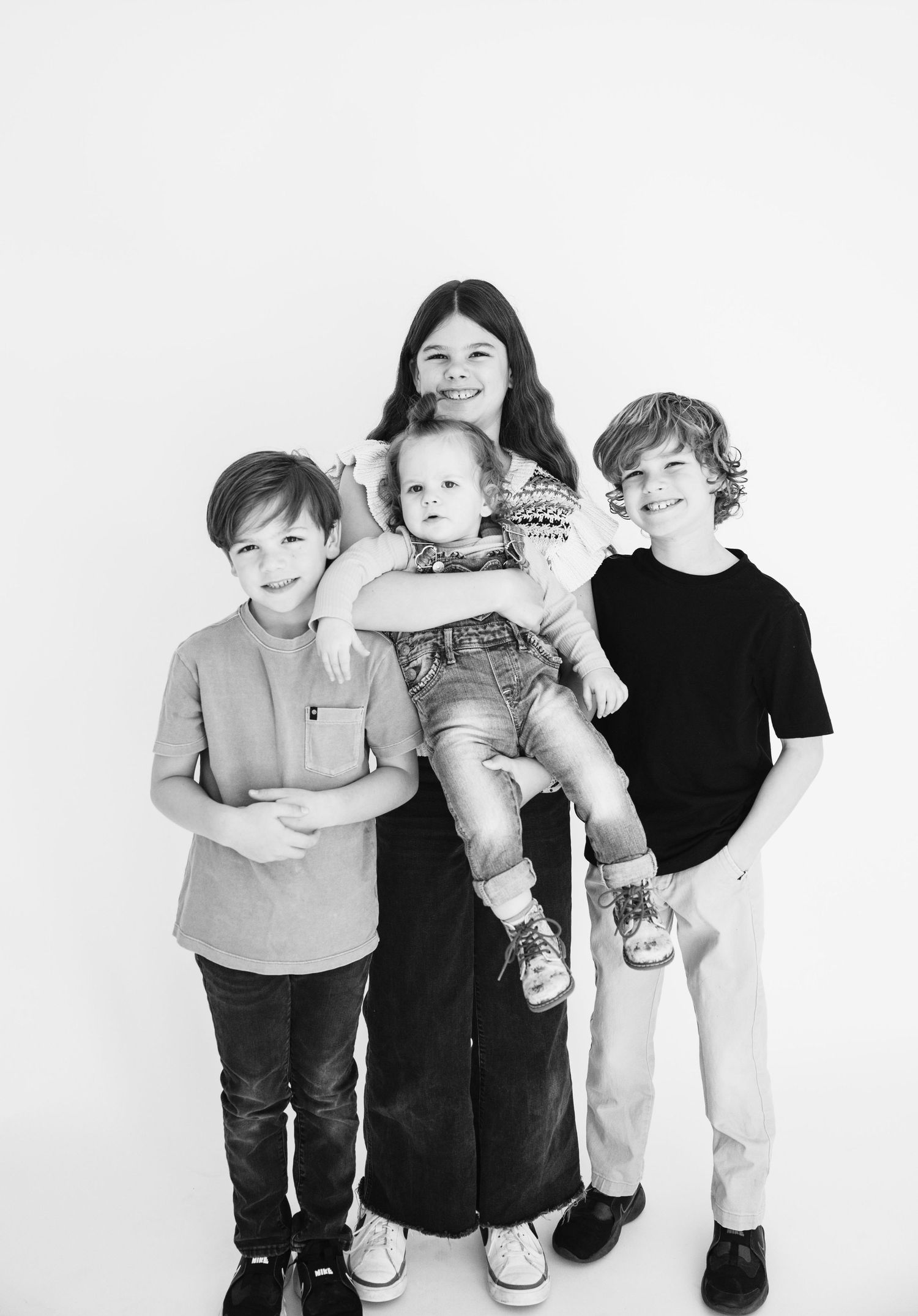 Black and white studio portrait of four siblings standing together against white background.