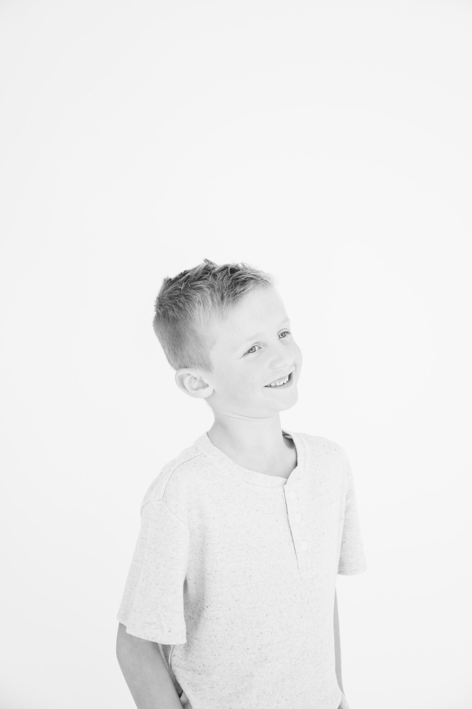 Black and white portrait of child in henley shirt with joyful expression.