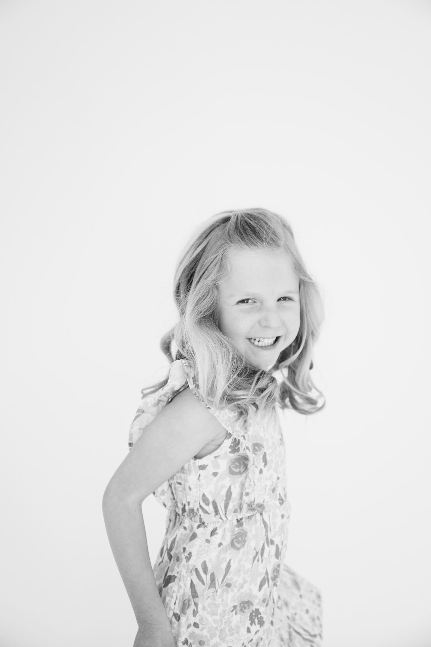 Black and white portrait of child in floral dress posing playfully.