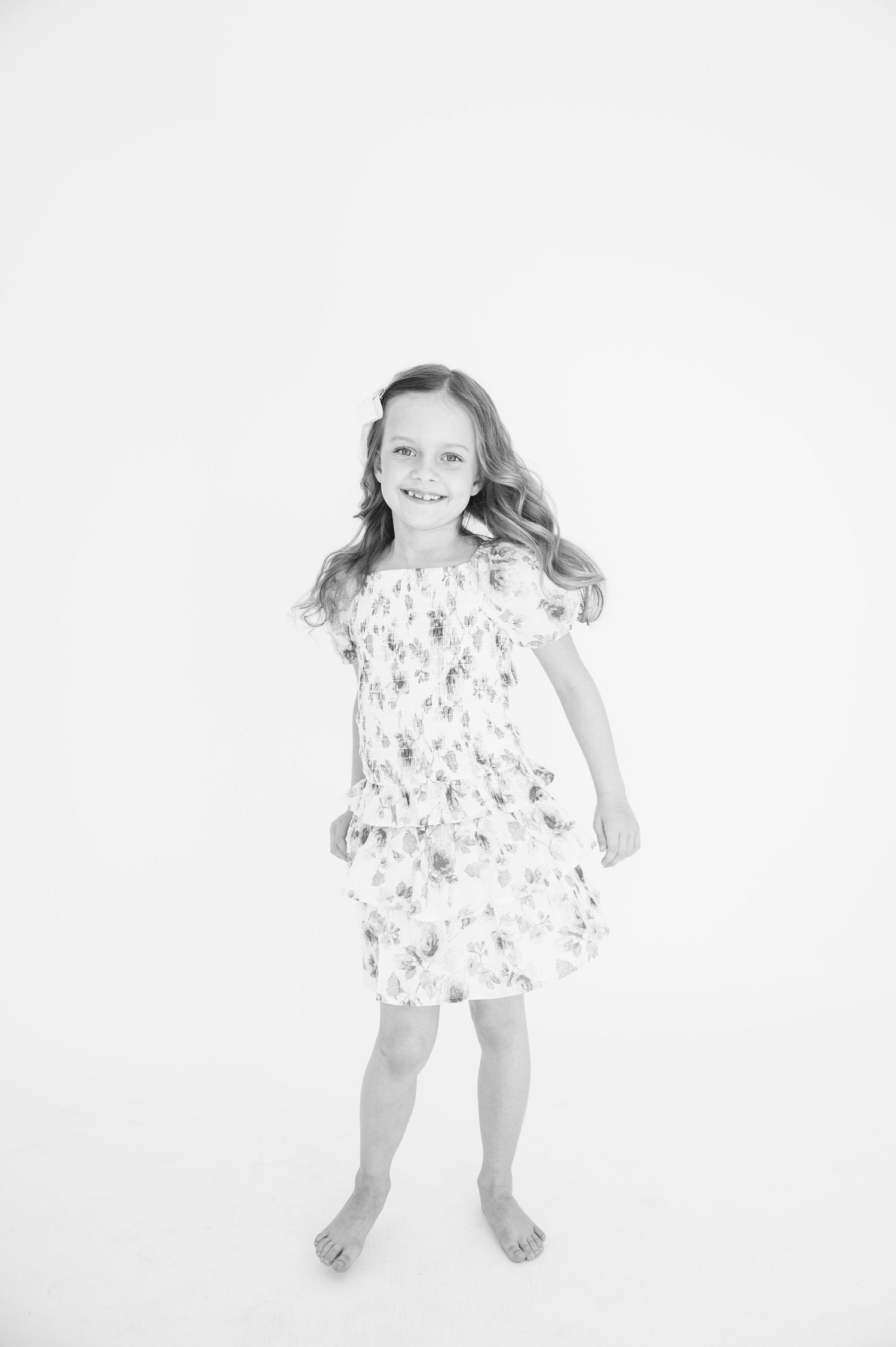 Black and white portrait of a smiling child in a floral dress against a white background.