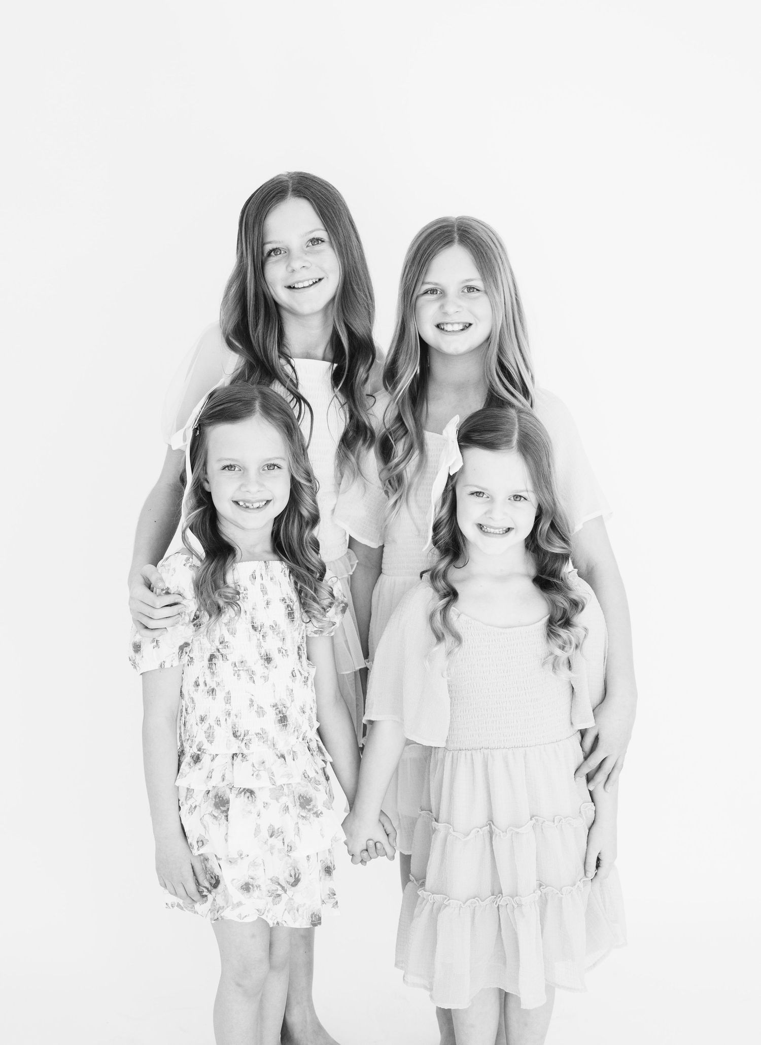 Black and white studio portrait of four individuals in light-colored dresses.