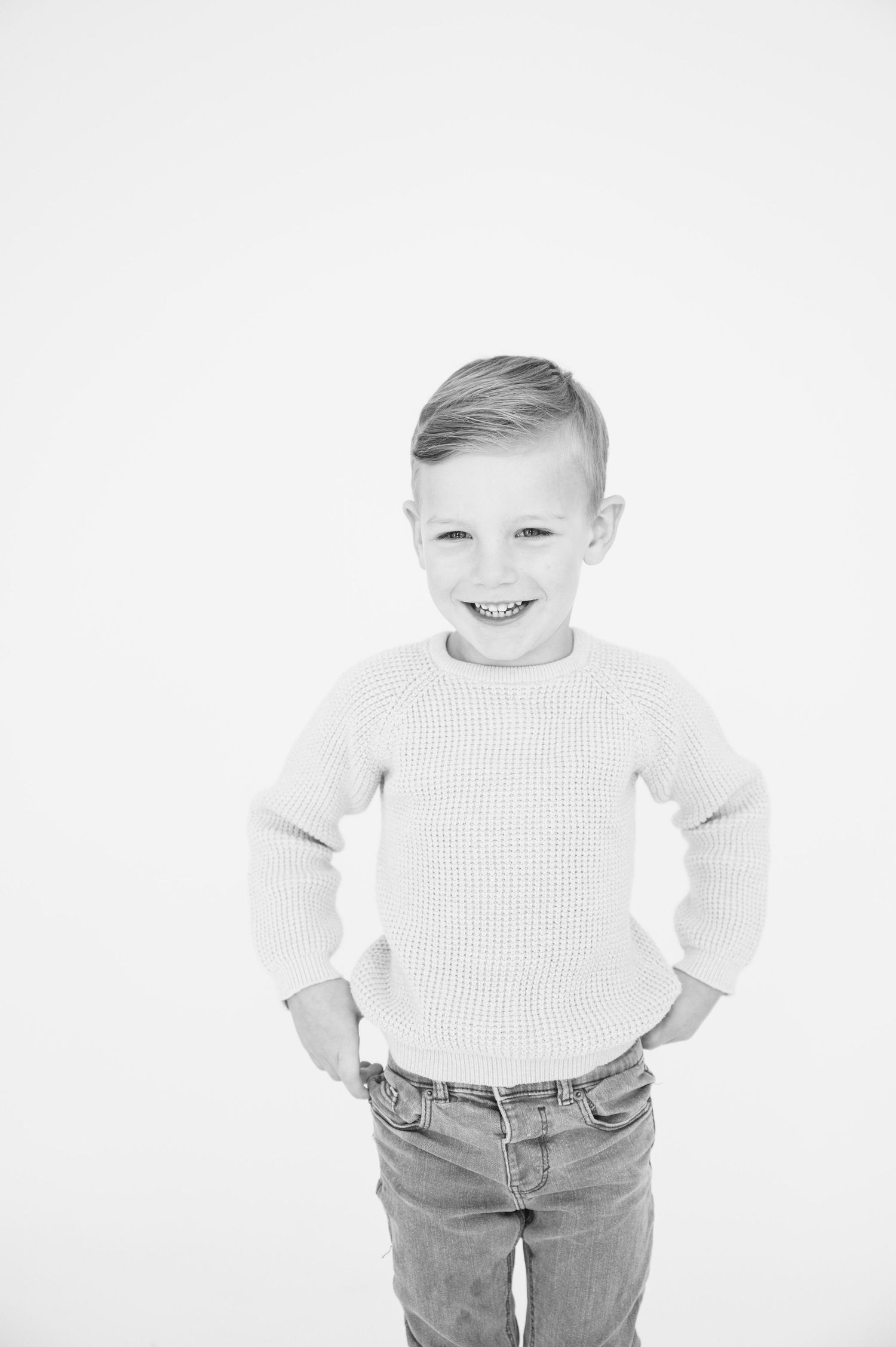 Black and white portrait of young person in sweater and jeans with hands on hips.