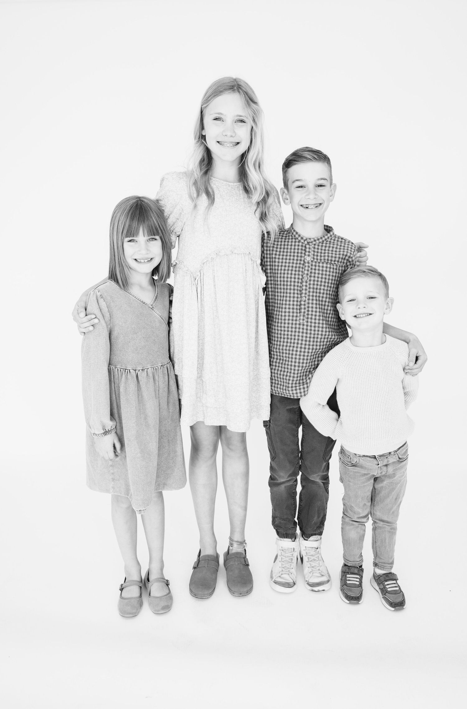 Black and white studio portrait of four siblings standing together against white background.