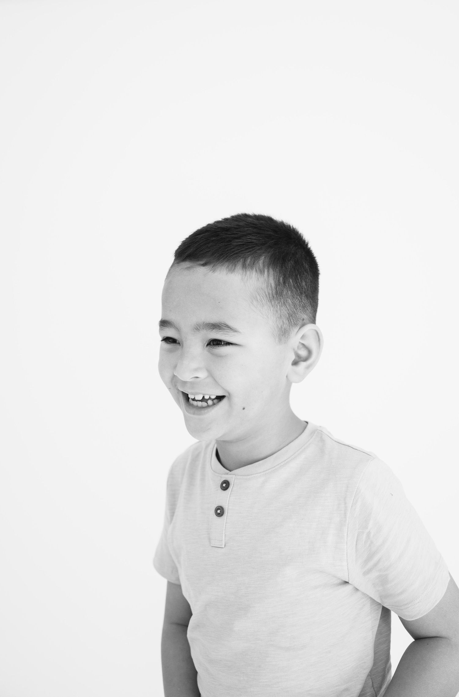 Black and white portrait of a child in a henley shirt smiling against white backdrop.
